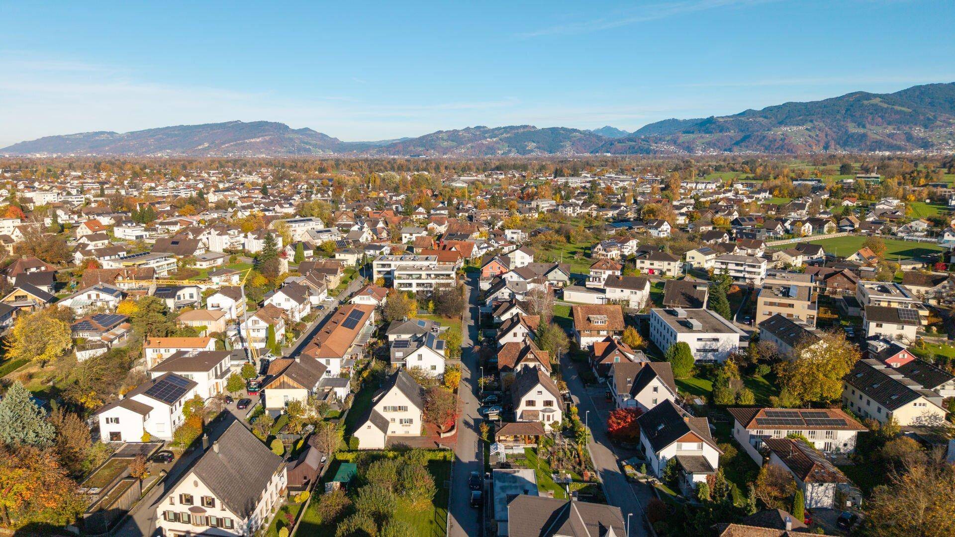 Panoramablick über eine Wohnsiedlung mit grünen Gärten und Bergen am Horizont.