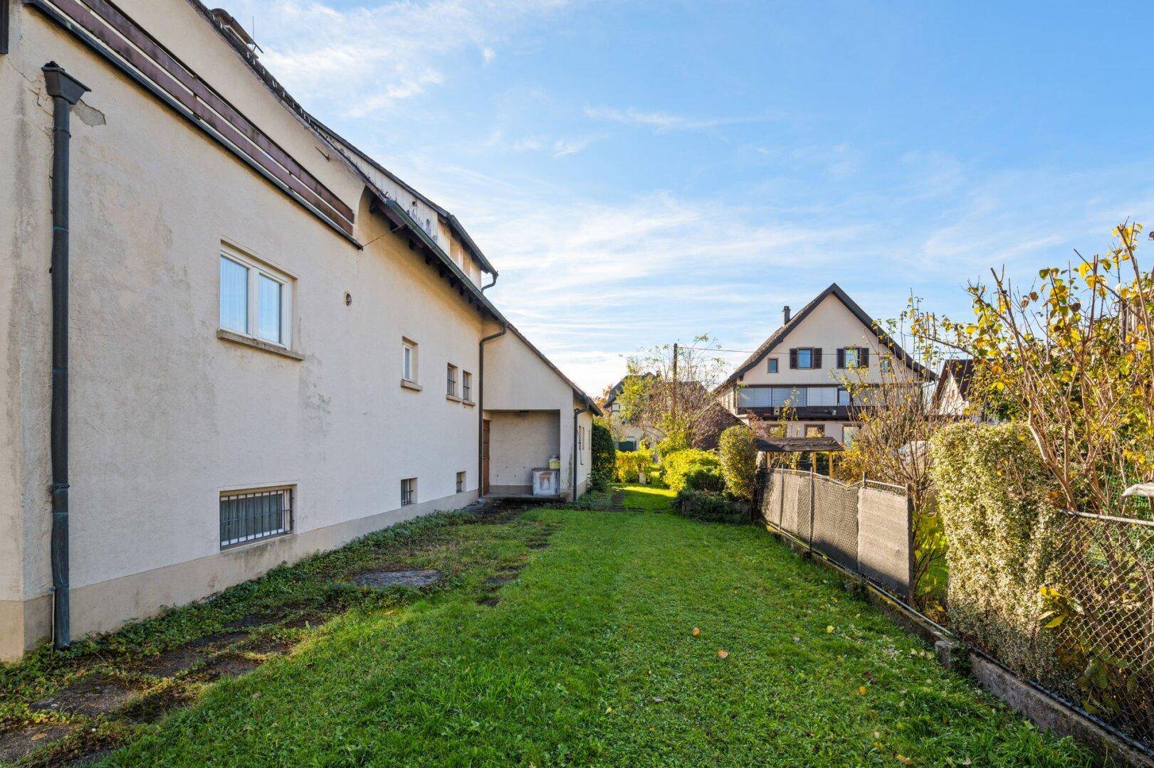 Lange Rasenfläche neben dem Haus mit Blick auf ein weiteres Gebäude im Hintergrund.