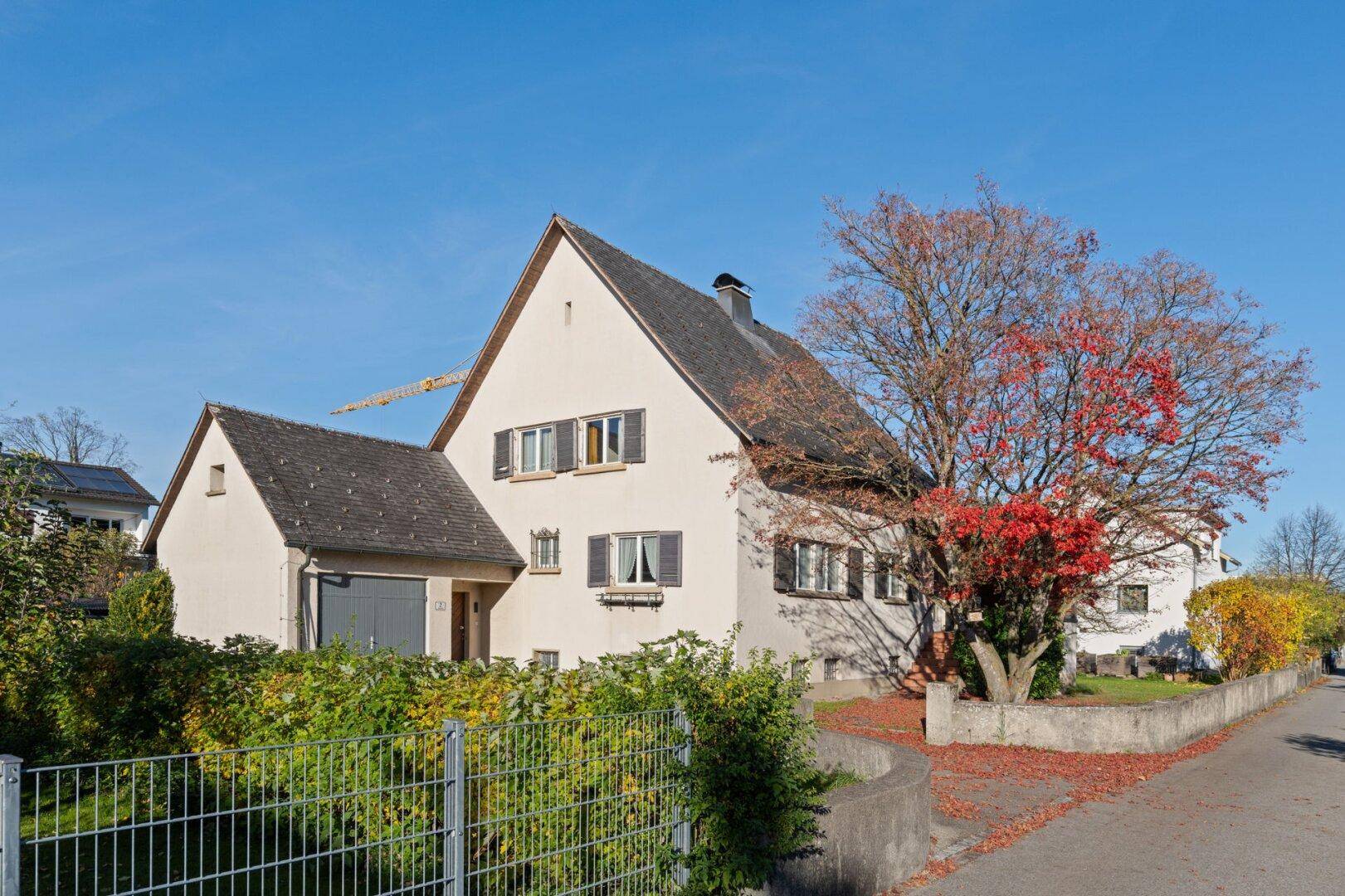 Ansicht des Hauses von der Straße mit Herbstlaub und einem Baum mit roten Blättern.