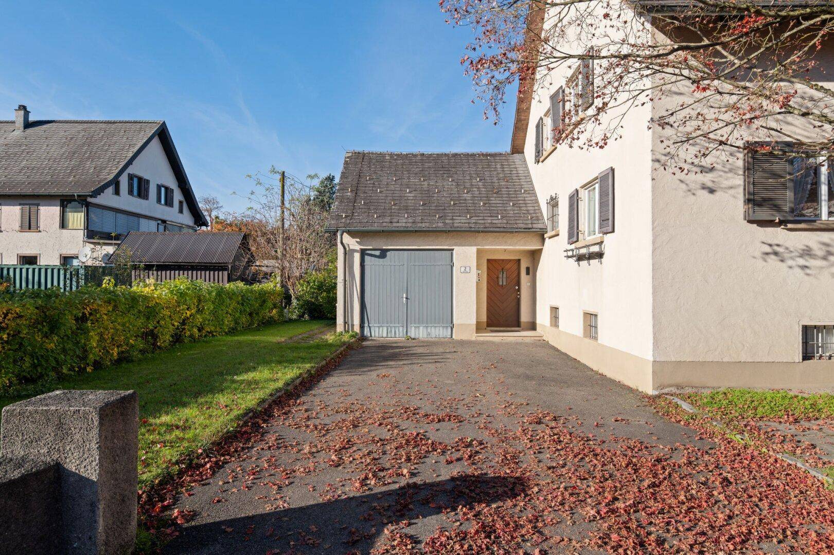 Vorderansicht des Hauses mit Einfahrt, Garage und Herbstlaub auf dem Boden.