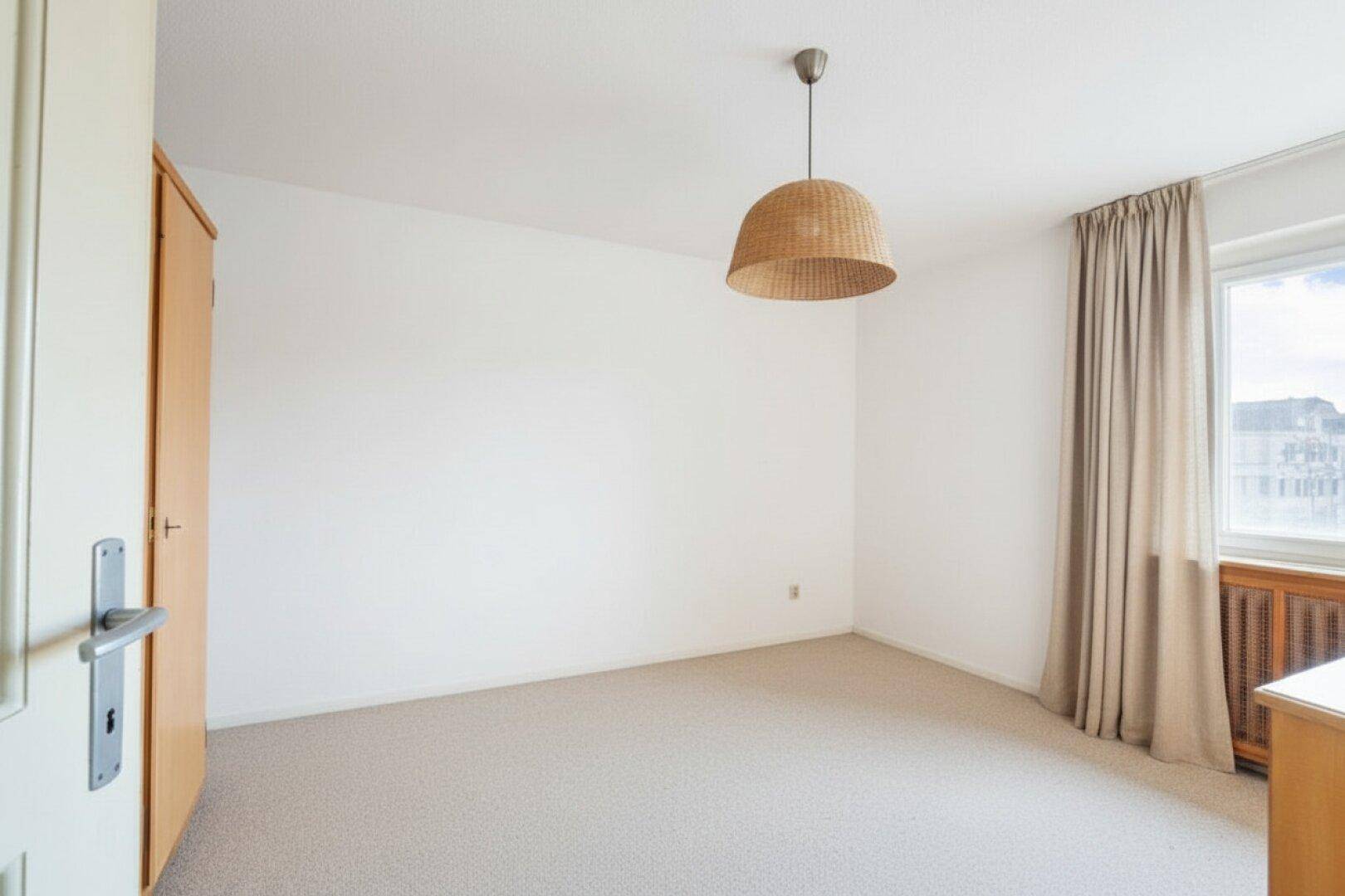 Helles Schlafzimmer mit Teppichboden, weiß gestrichenen Wänden und Fenster.
