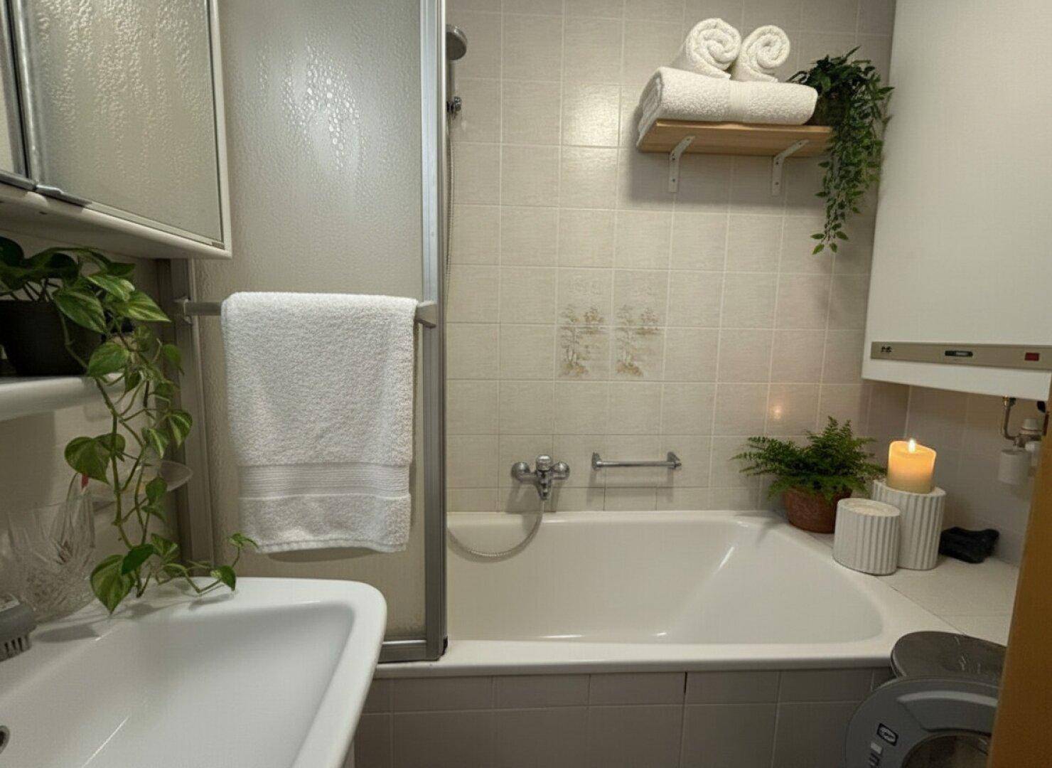 Badezimmer mit Badewanne, Duschabtrennung und hellen Fliesen.