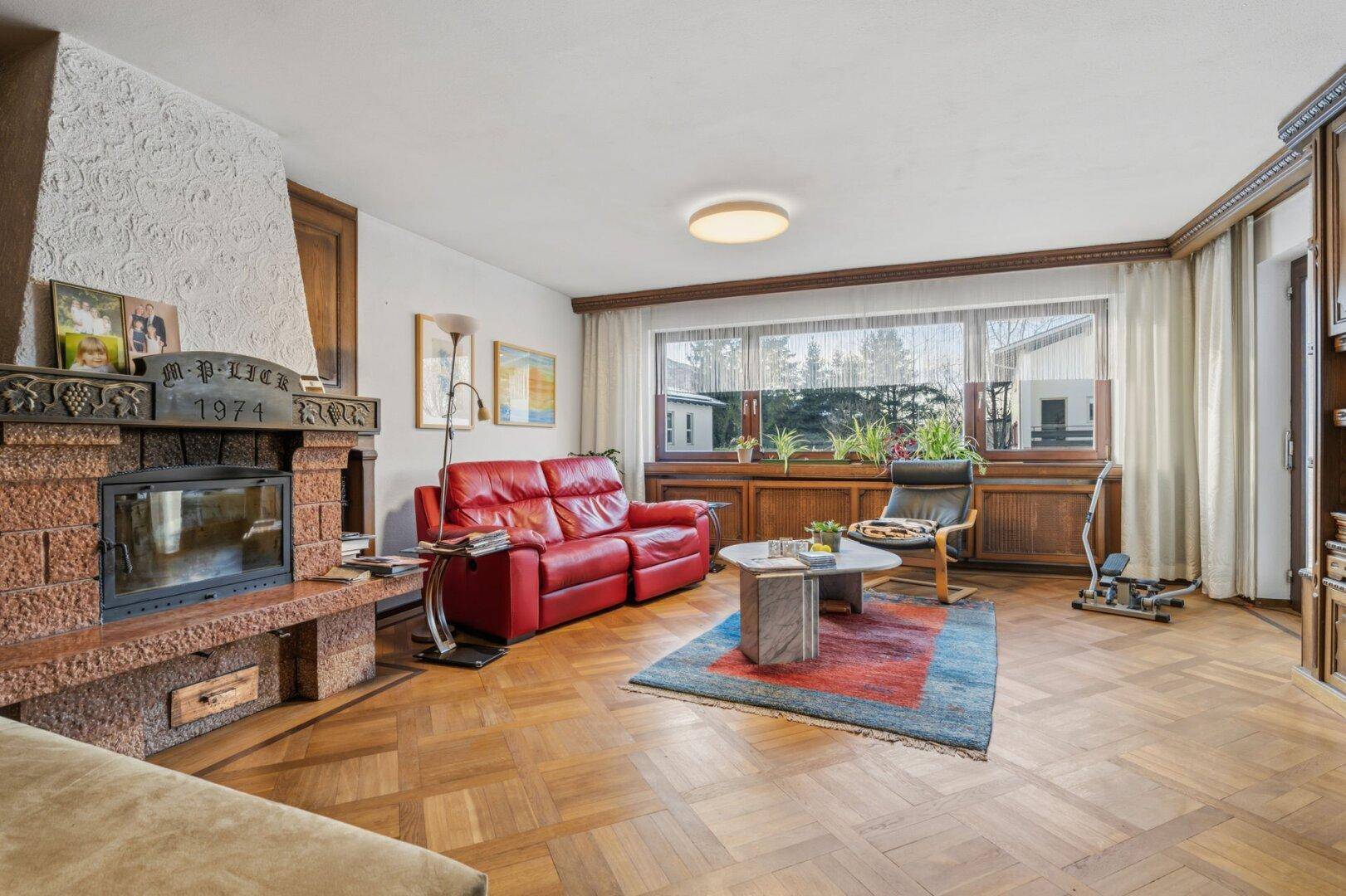 Gemütliches Wohnzimmer mit Parkettboden, Kamin und rotem Sofa, umgeben von Holzvertäfelung.
