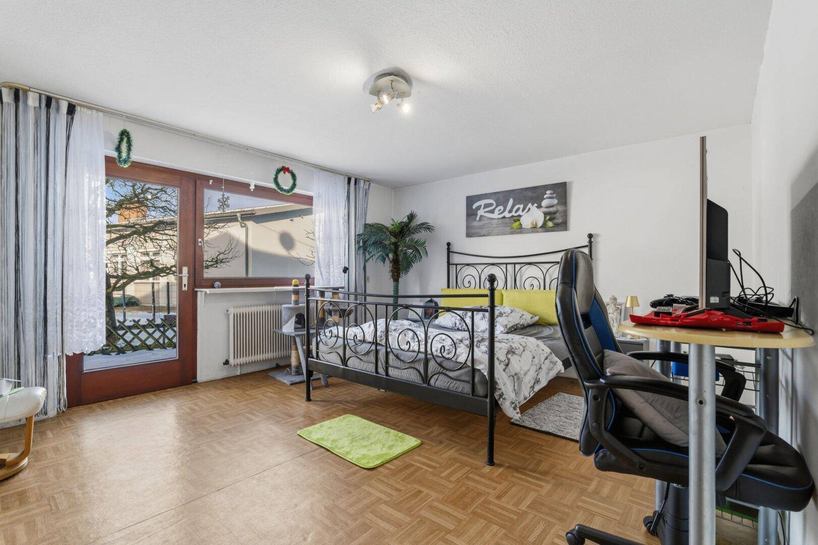 Schlafzimmer mit Parkettboden, Balkonzugang und Blick ins Freie.