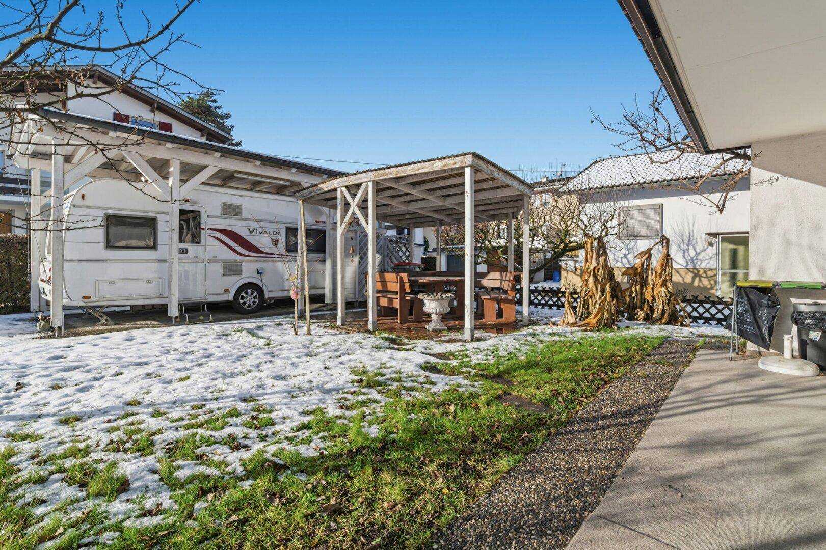 Gartenbereich mit Rasenfläche, Pergola und Stellplatz für einen Wohnwagen.