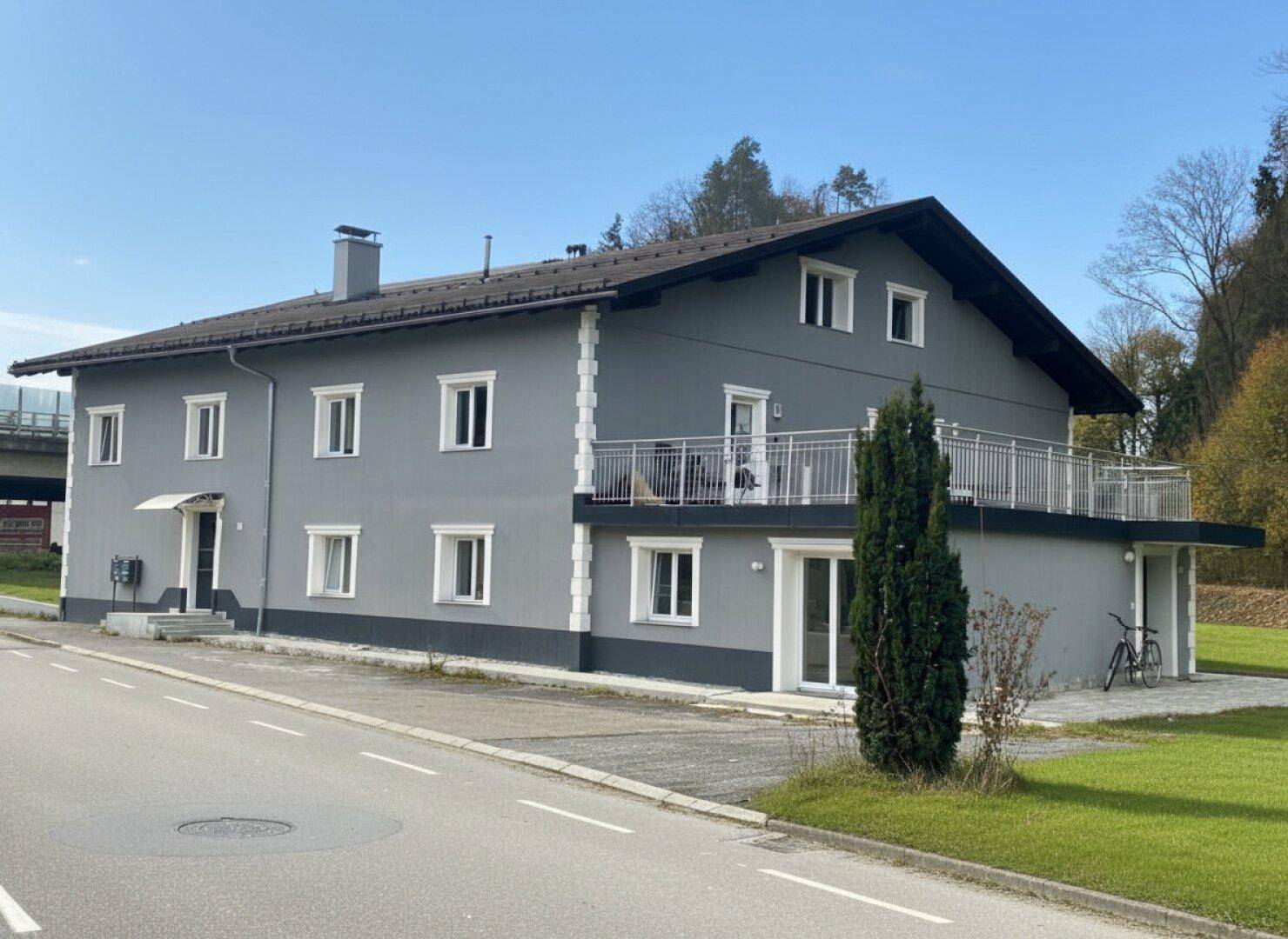 Ansicht des grauen Gebäudes mit Balkon und weiß gerahmten Fenstern an einer Straße gelegen.