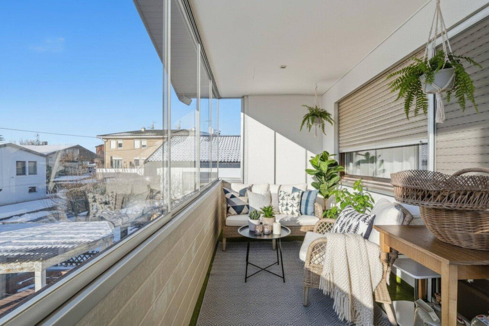 Verglaster Balkon mit gemütlicher Sitzecke und Blick auf die verschneite Umgebung.