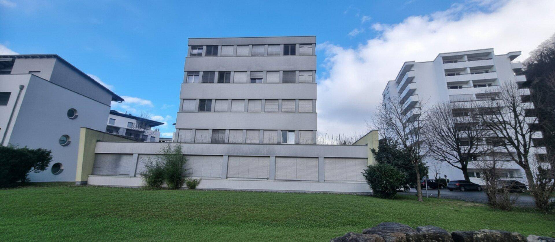 Mehrstöckiges Gebäude mit schlichter Fassade, umgeben von Grünflächen und weiteren Wohngebäuden.
