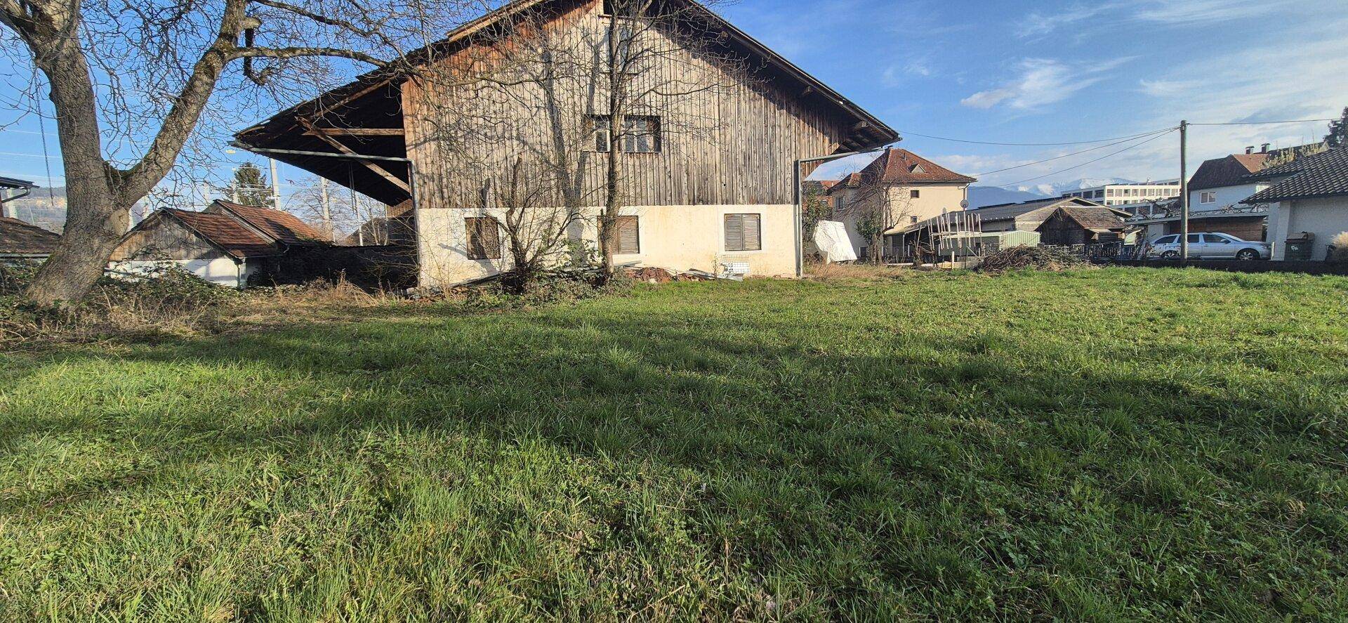Gesamtansicht des alten Gebäudes mit seiner Holzfassade und dem großen, sonnigen Grundstück.