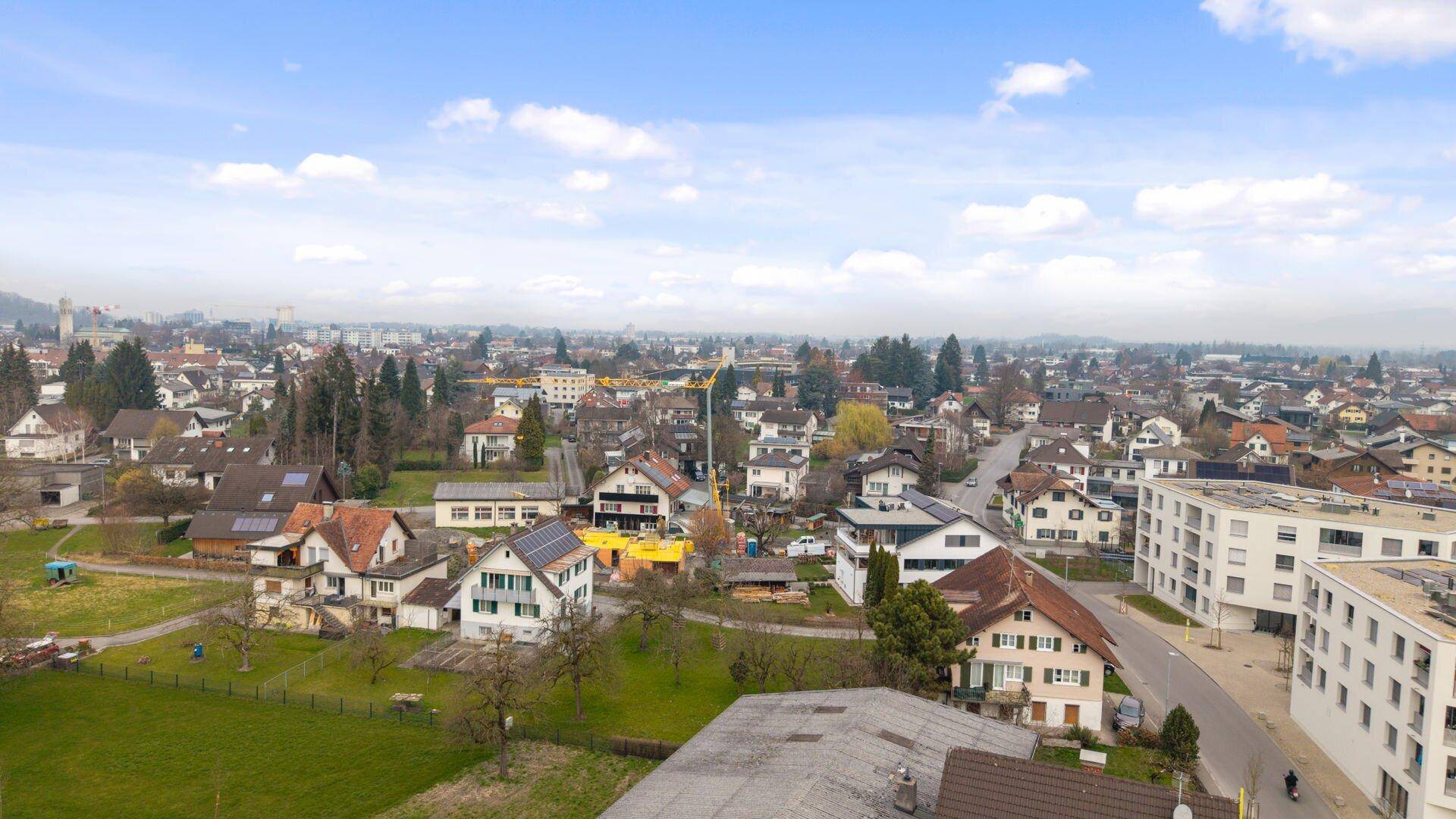 Weitläufige Luftaufnahme eines Wohnviertels mit Häusern, Gärten und einem weiten Blick in die Landschaft.