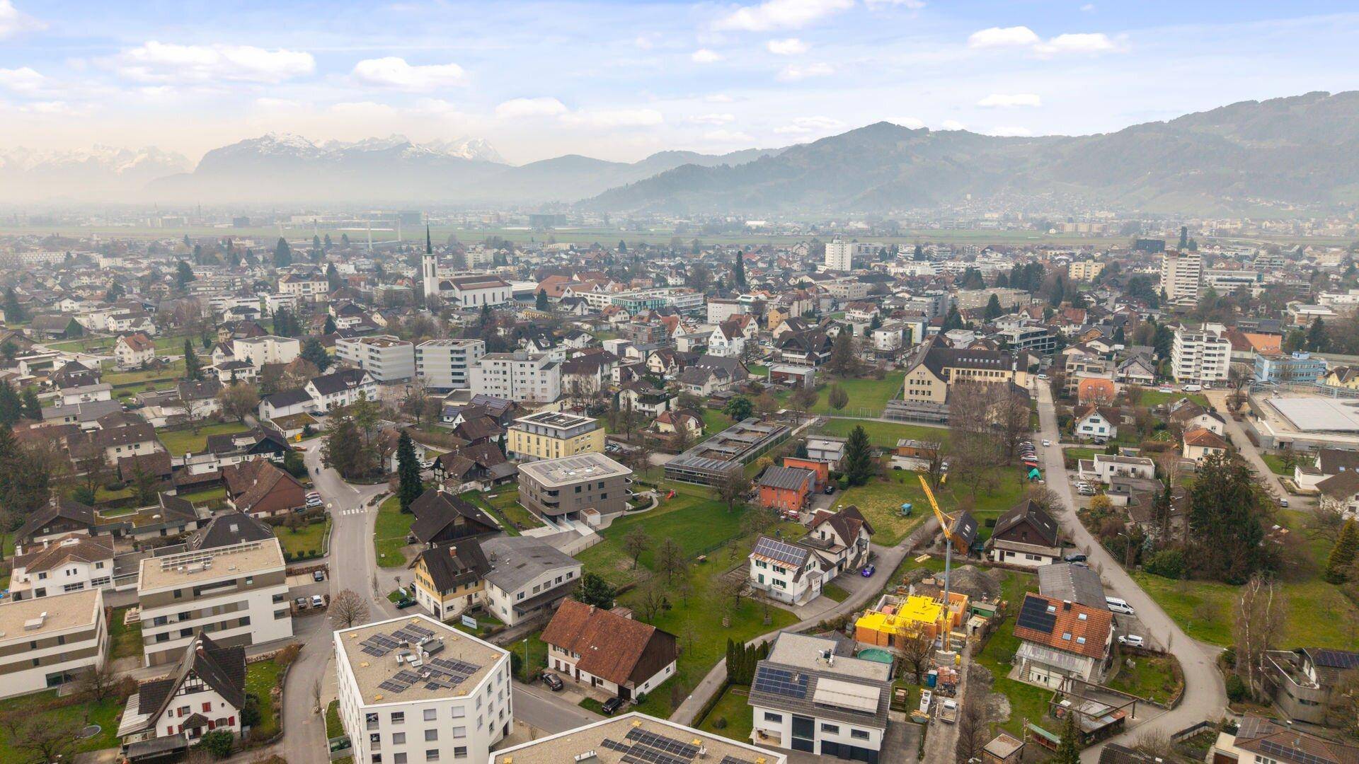 Weitläufige Luftaufnahme einer Stadt mit Wohngebieten und einer beeindruckenden Bergkulisse im Hintergrund.