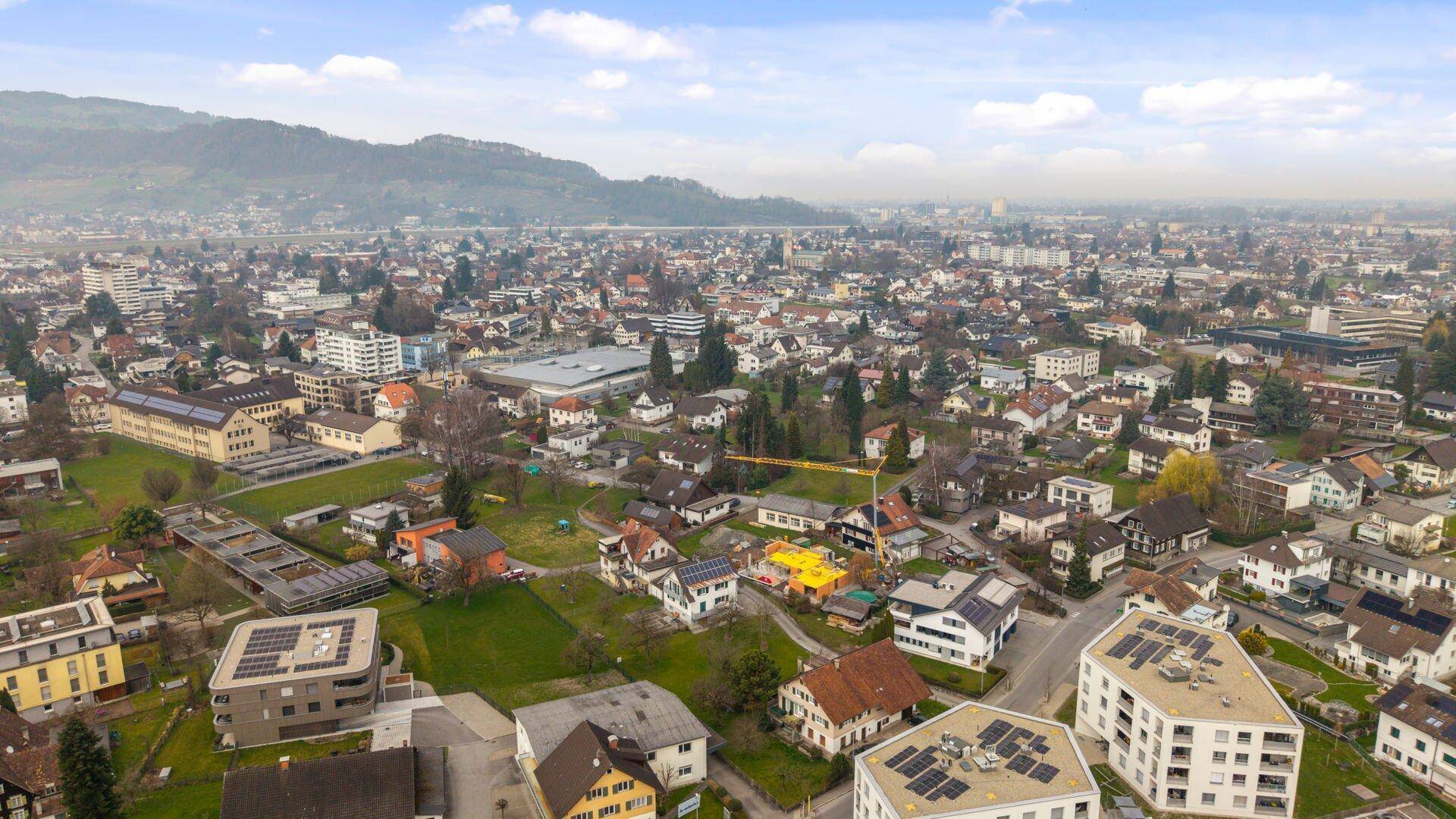 Luftaufnahme einer städtischen Siedlung mit vielfältiger Bebauung und einem weiten Blick auf die umliegende Landschaft.