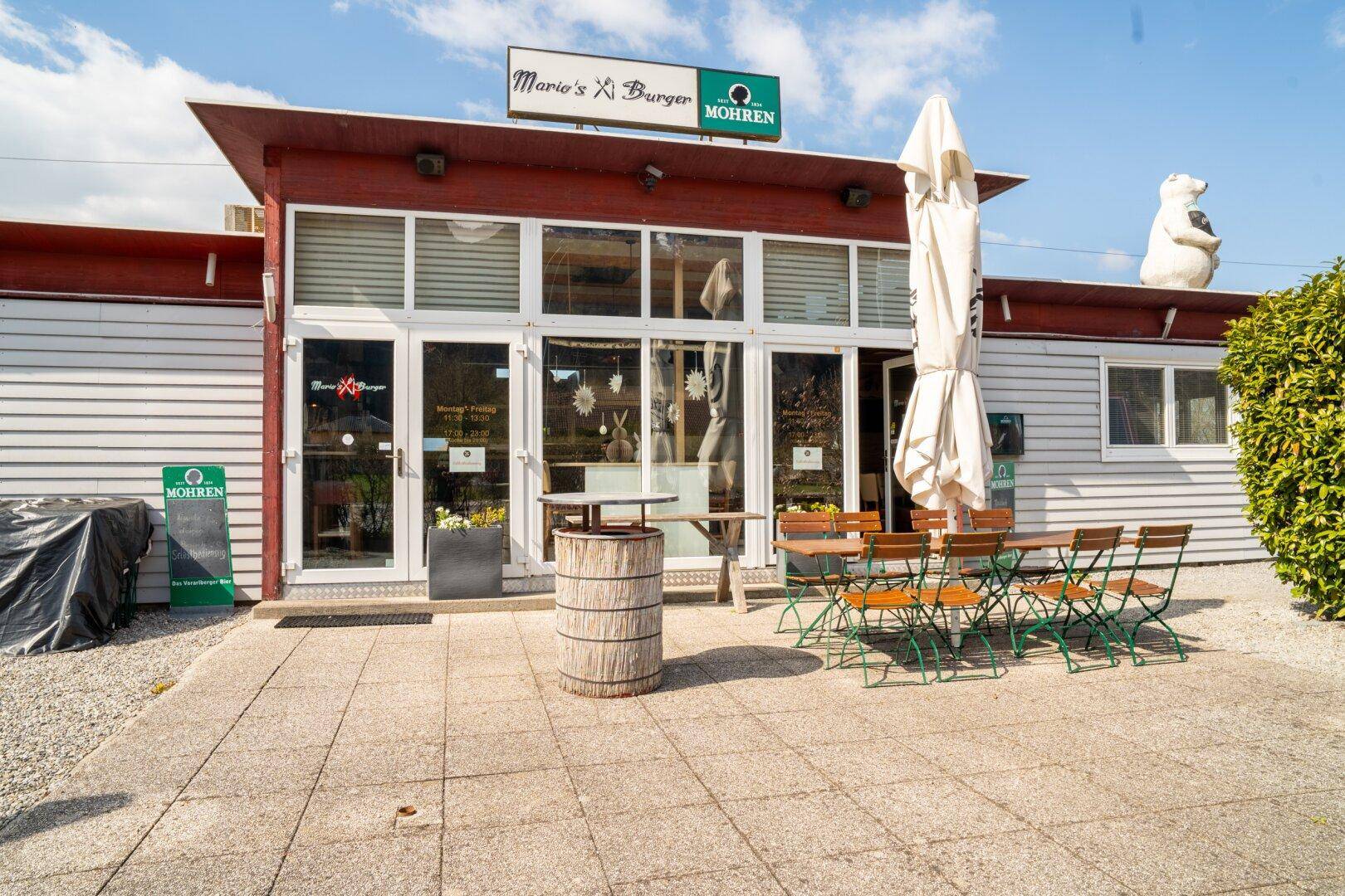 Außenansicht eines Restaurants mit Terrasse, Sonnenschirm und Sitzgelegenheiten im Freien.