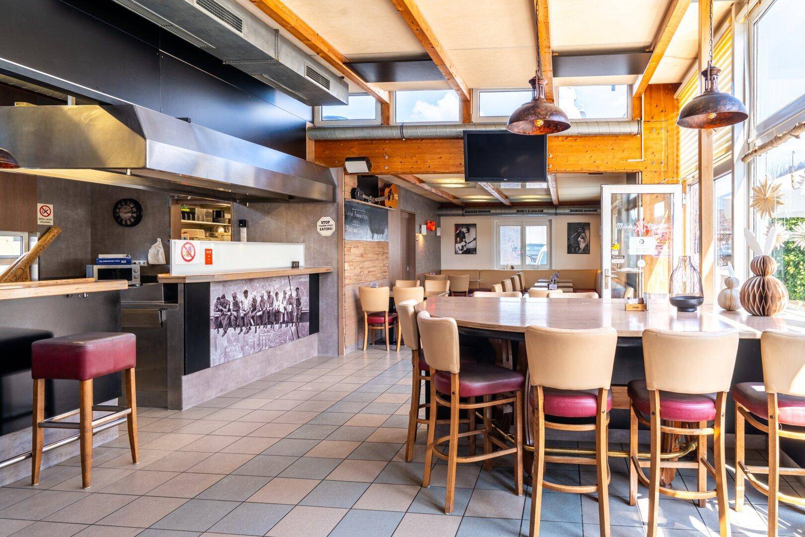 Geräumiger Restaurantbereich mit offener Küche, Holzbalken und verschiedenen Sitzgelegenheiten.