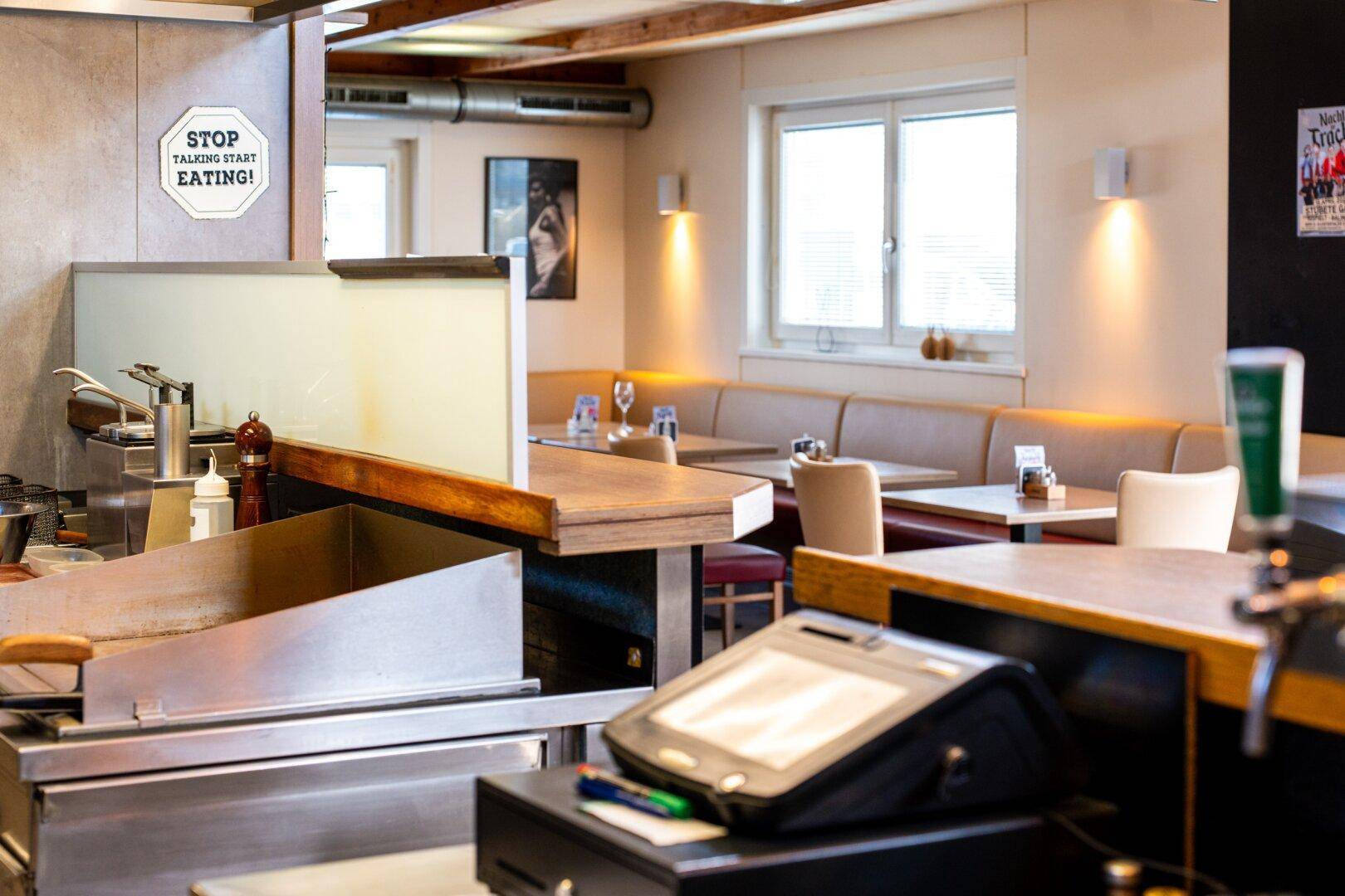 Thekenbereich mit Grillstation und Blick in den hellen Gastraum mit Sitzgelegenheiten.