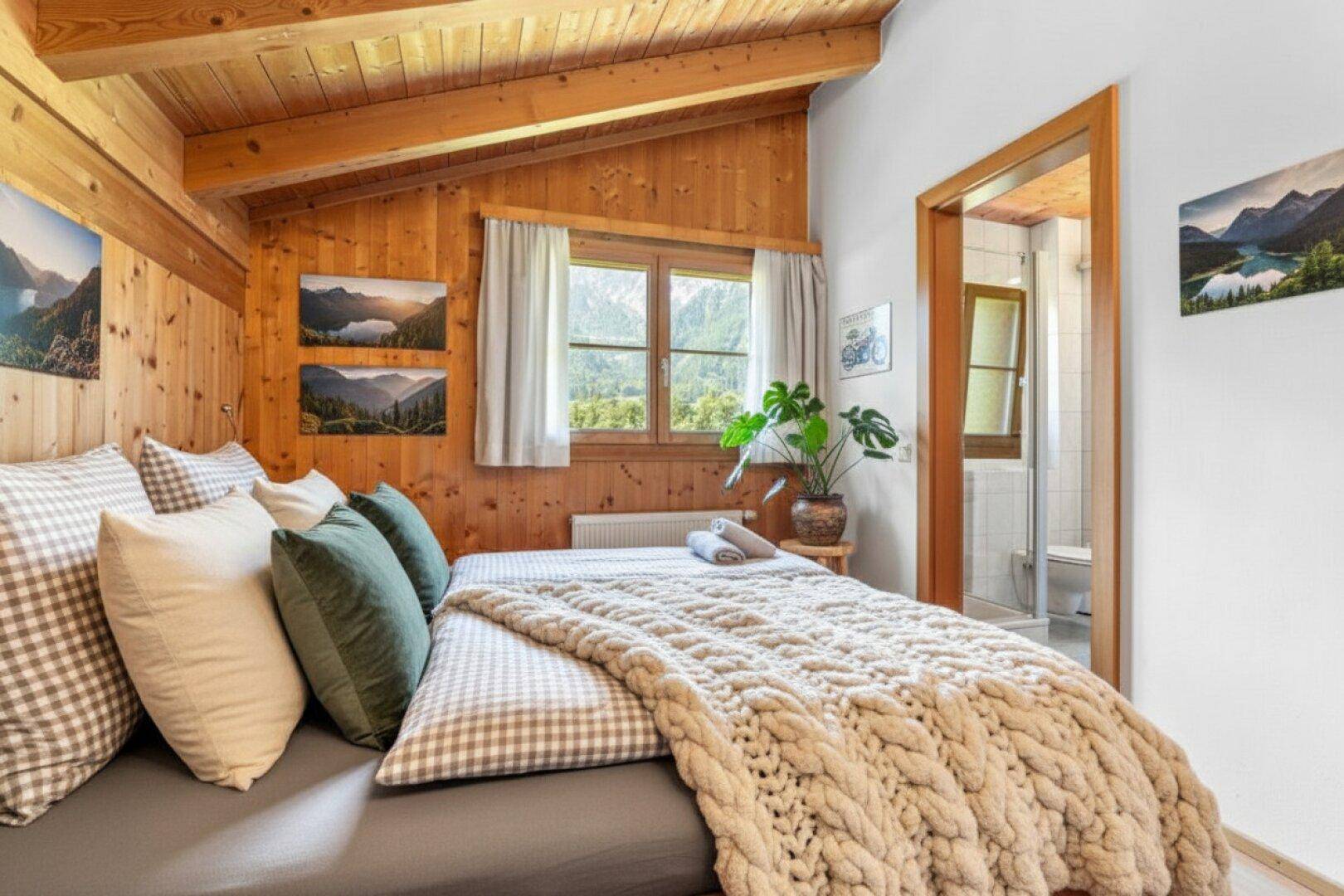 Helles Schlafzimmer mit Holzwänden, Holzbalkendecke und direktem Zugang zum Badezimmer.