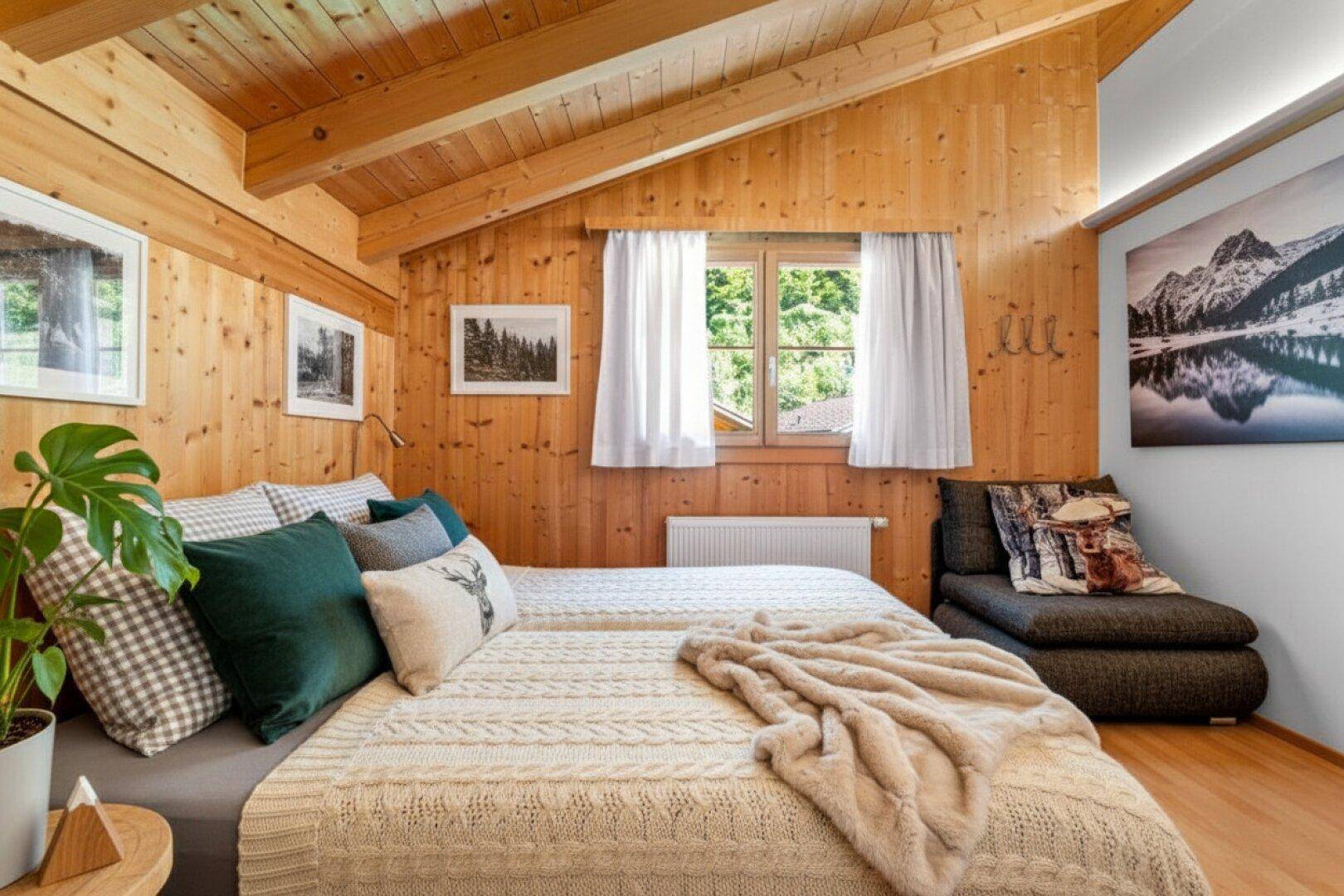 Gemütliches Schlafzimmer mit Holzwänden, Holzbalkendecke und Blick ins Grüne.