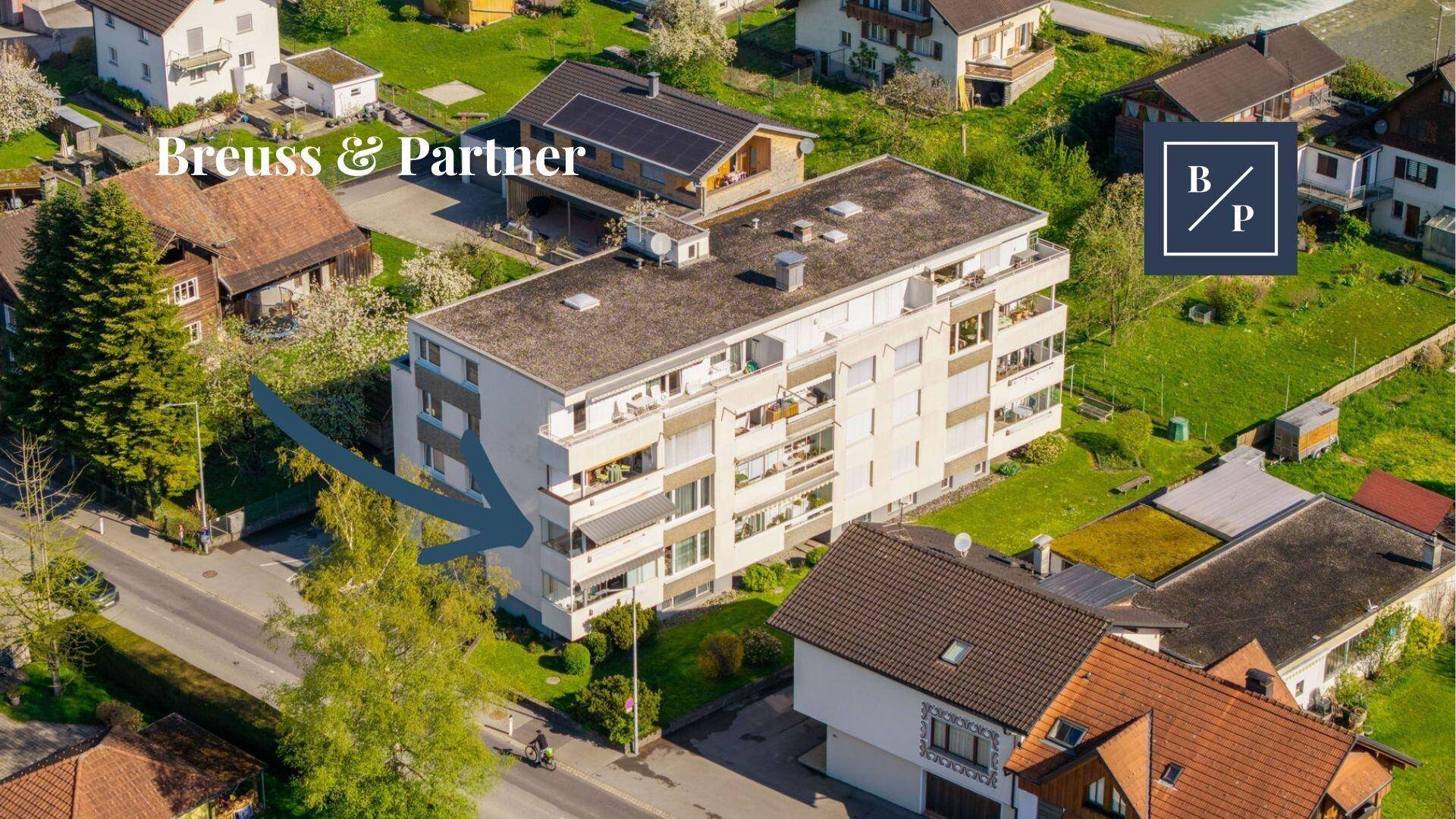Luftaufnahme eines Mehrfamilienhauses mit Balkonen in grüner Umgebung.