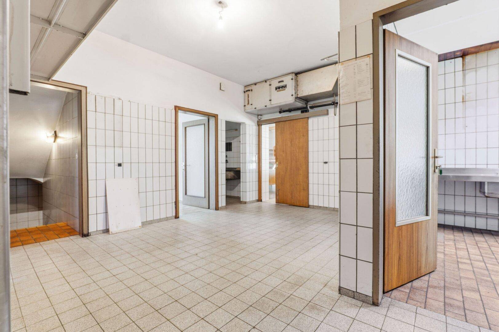 Großer gefliester Raum mit mehreren Türen und sichtbaren Lüftungsanlagen an der Decke.