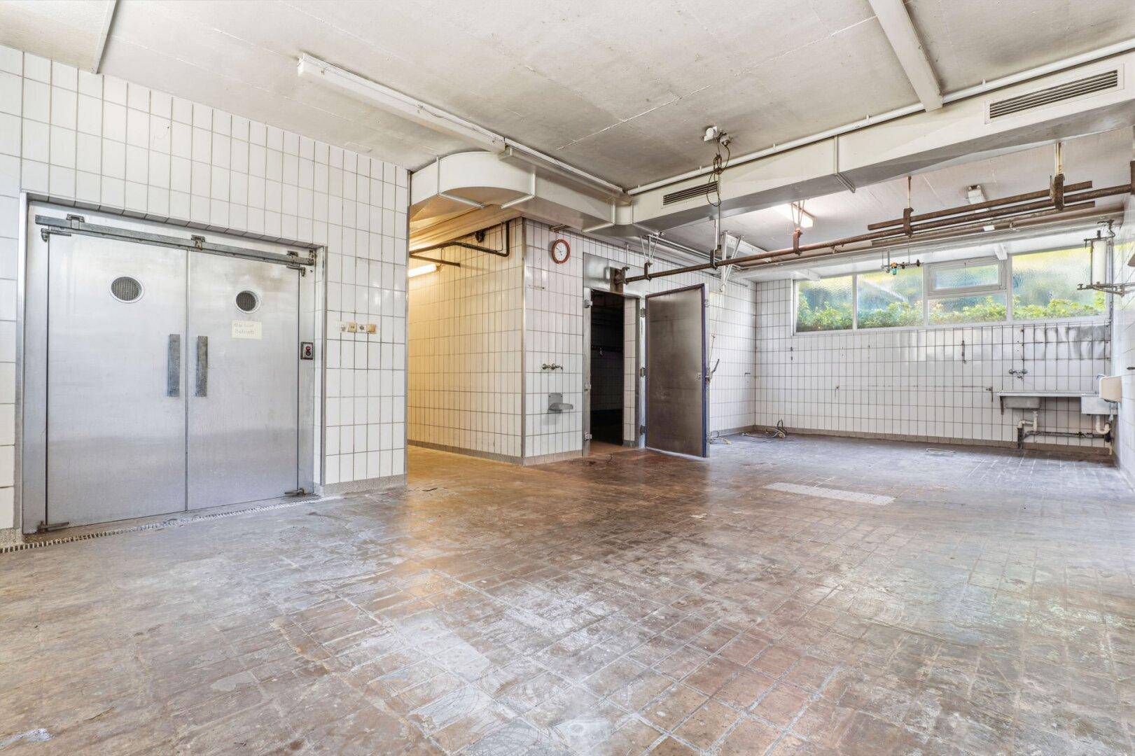 Großer gefliester Kellerraum mit Metalltüren und Fenstern, die Tageslicht hereinlassen.