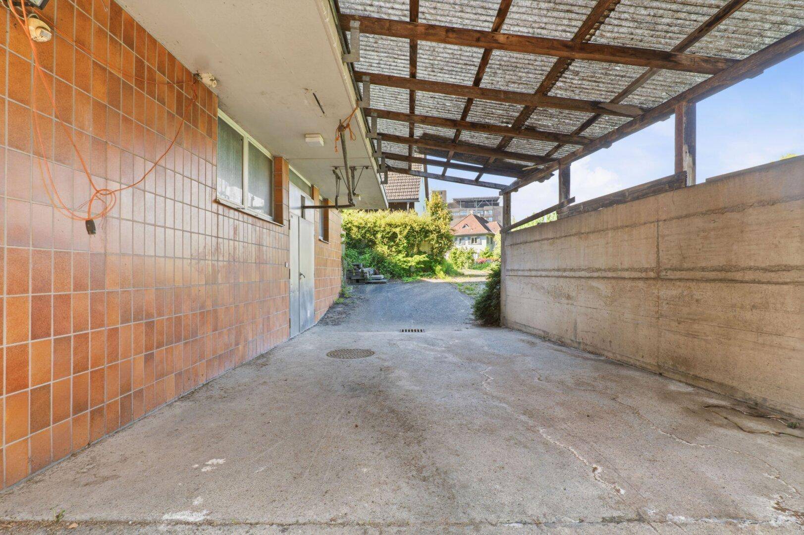 Überdachter Außenbereich mit gefliester Wand und Blick auf eine Zufahrt.