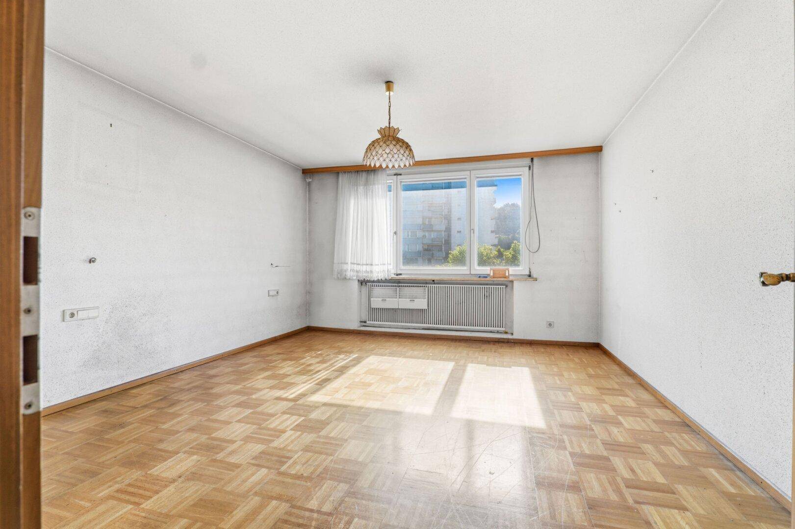 Helles Zimmer mit Parkettboden, großem Fenster und viel natürlichem Licht, bereit zur Einrichtung.