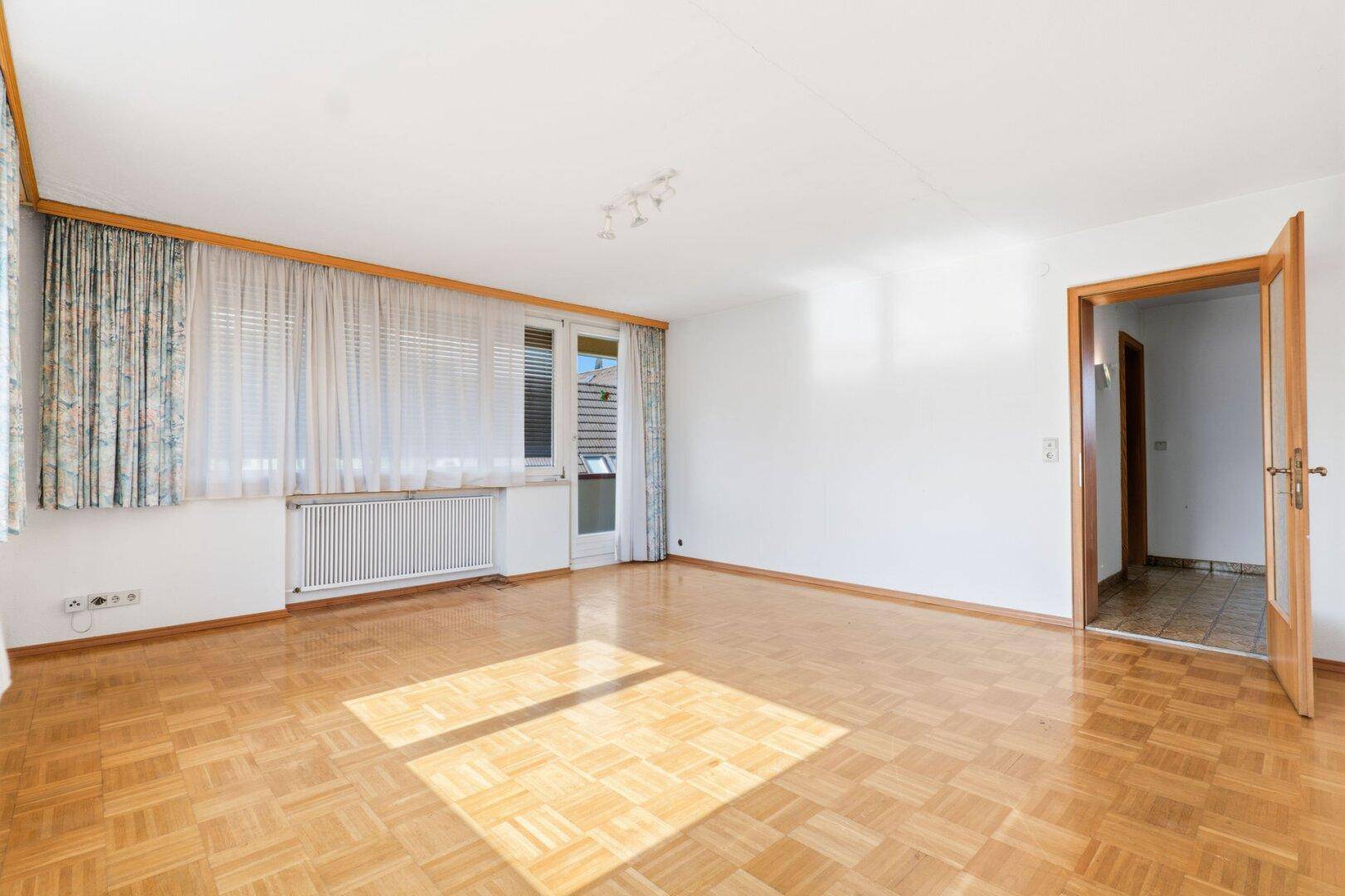 Heller Wohnraum mit Parkettboden und direktem Zugang zu einem Balkon oder einer Terrasse.