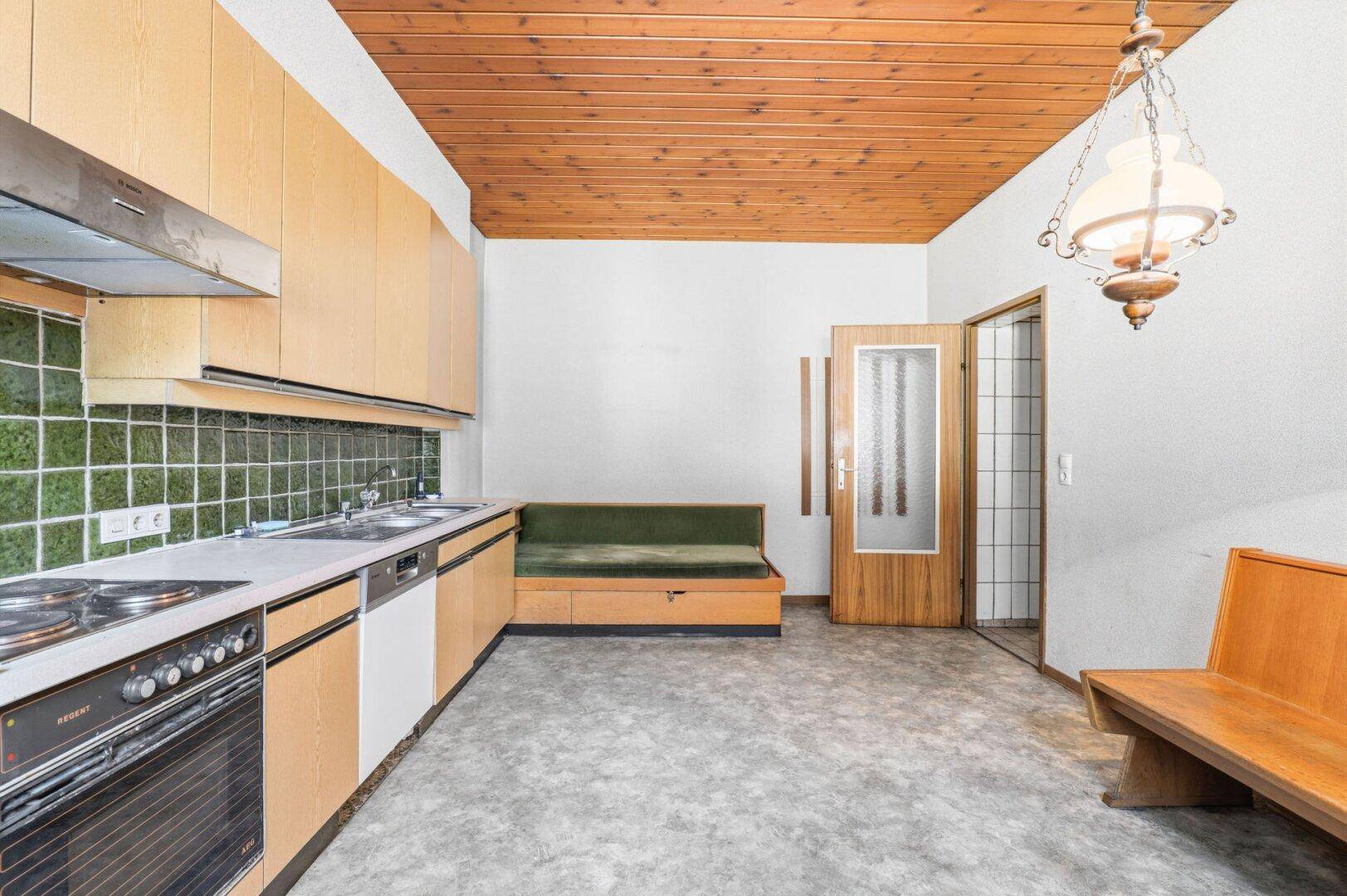 Küche mit hellen Holzschränken, grünen Fliesen und einer Holzdecke, inklusive Essbereich.
