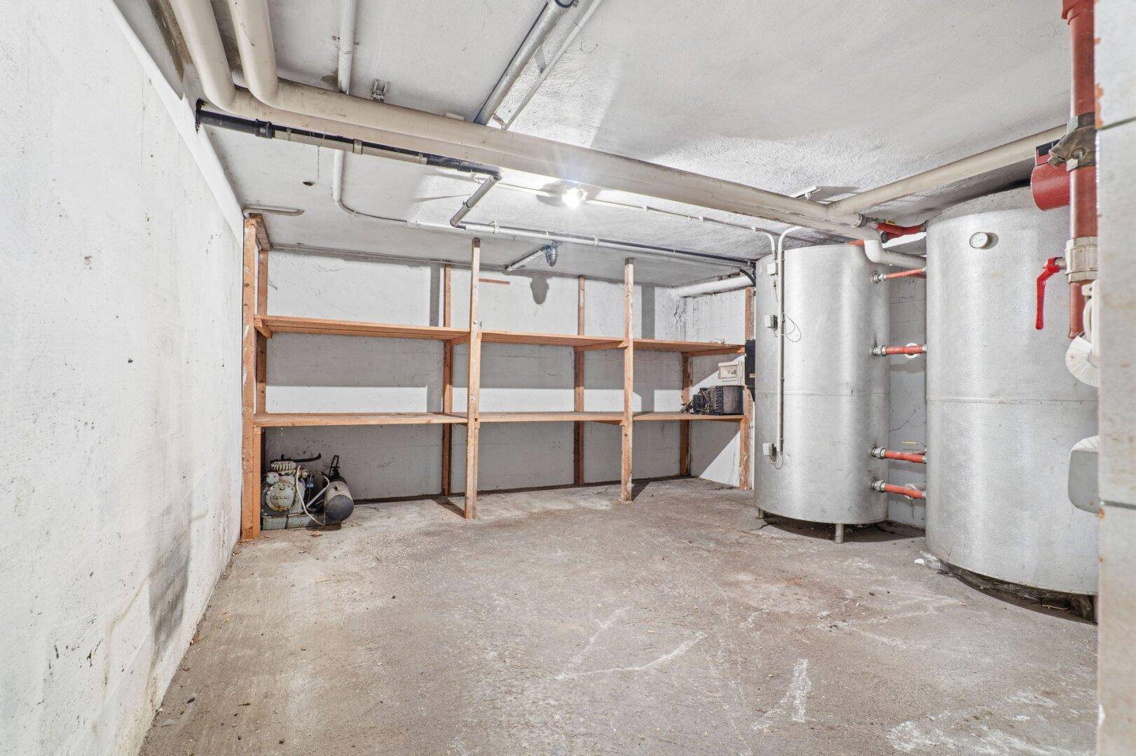 Hauswirtschaftsraum im Keller mit Betonboden, Regalen und großen Warmwasserspeichern.
