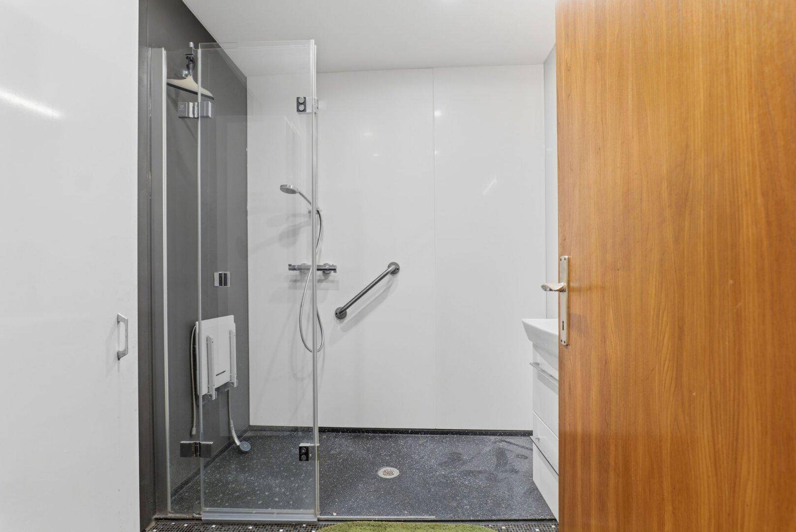 Badezimmer mit begehbarer Dusche, weißen und grauen Wänden sowie einem dunklen Musterboden.