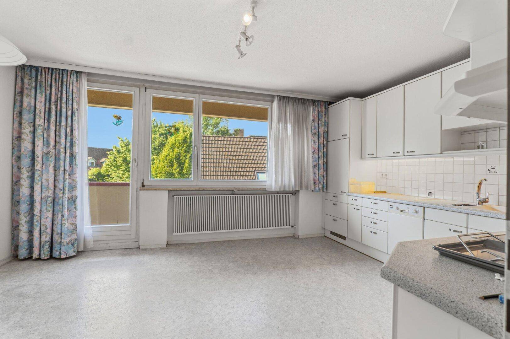 Helle Küche mit weißen Schränken, Vinylboden und Zugang zu einem kleinen Balkon.