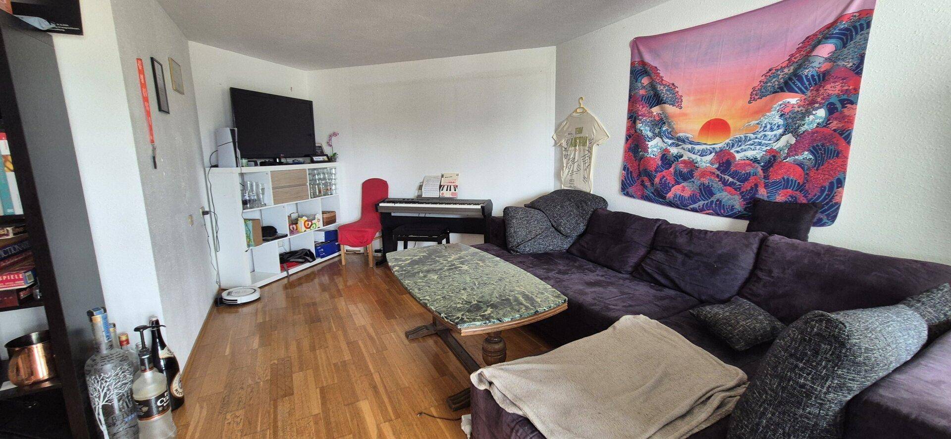 Wohnzimmer mit dunklem Sofa, Fernseher und farbenfroher Wanddekoration.