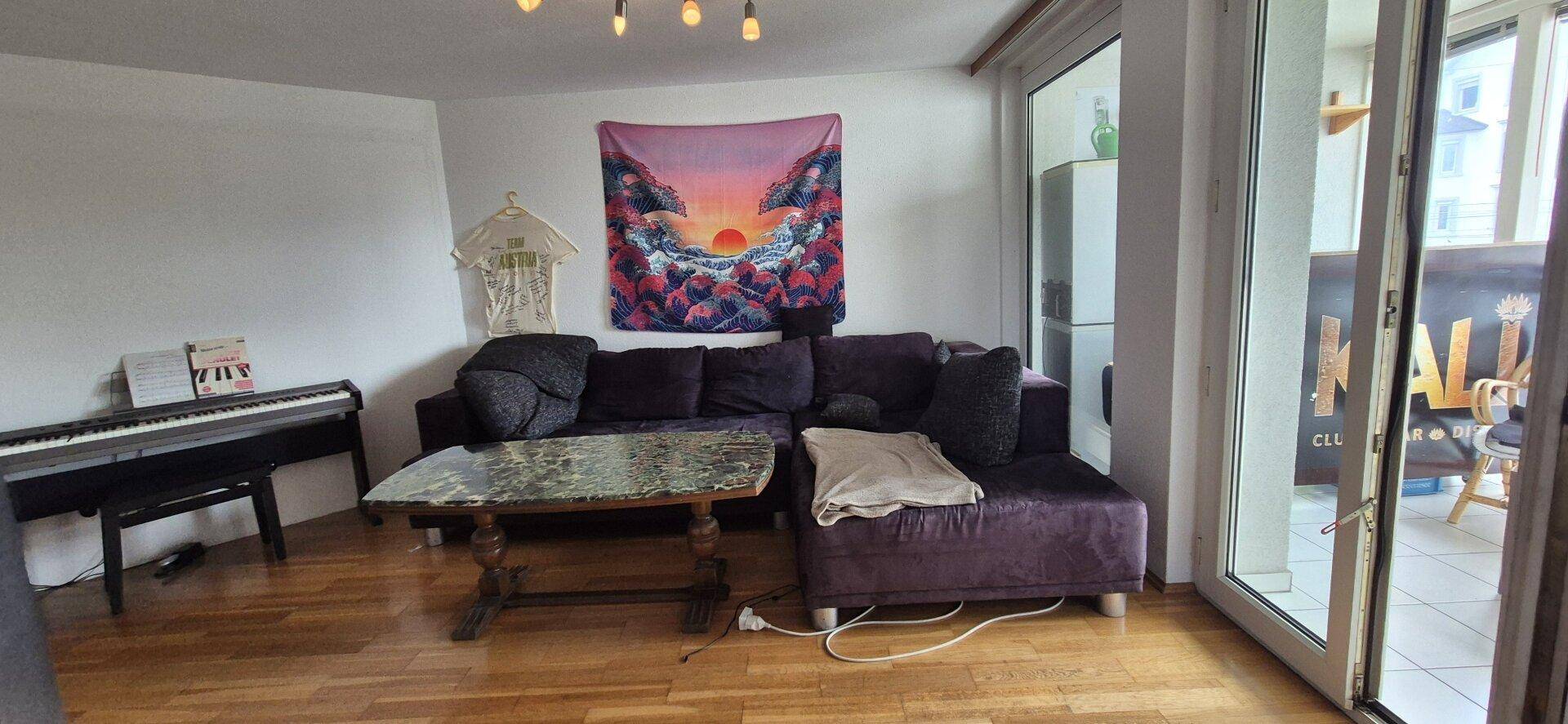 Wohnzimmer mit Sofa, Klavier und Zugang zum verglasten Balkon.