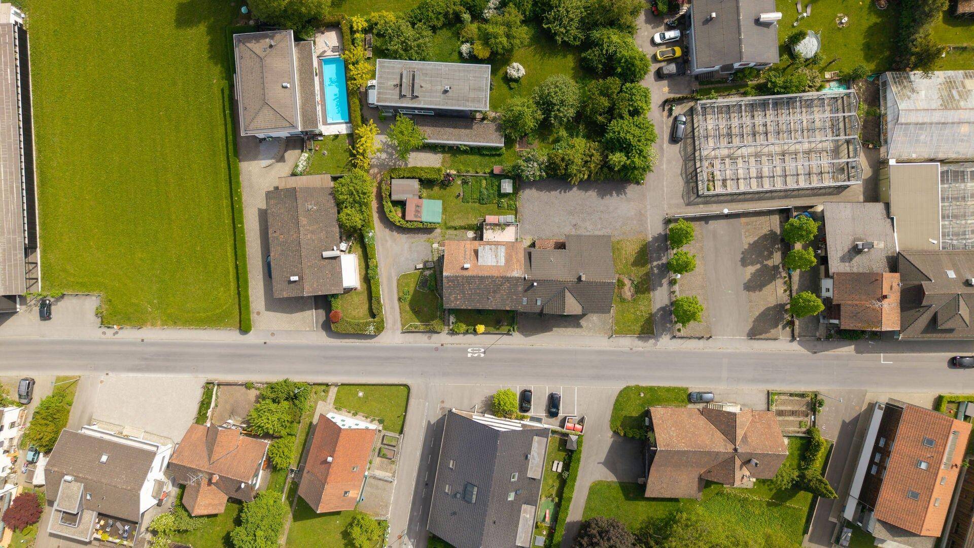 Vogelperspektive einer Wohnstraße mit Häusern, Gärten und einem Swimmingpool in einem Hinterhof.