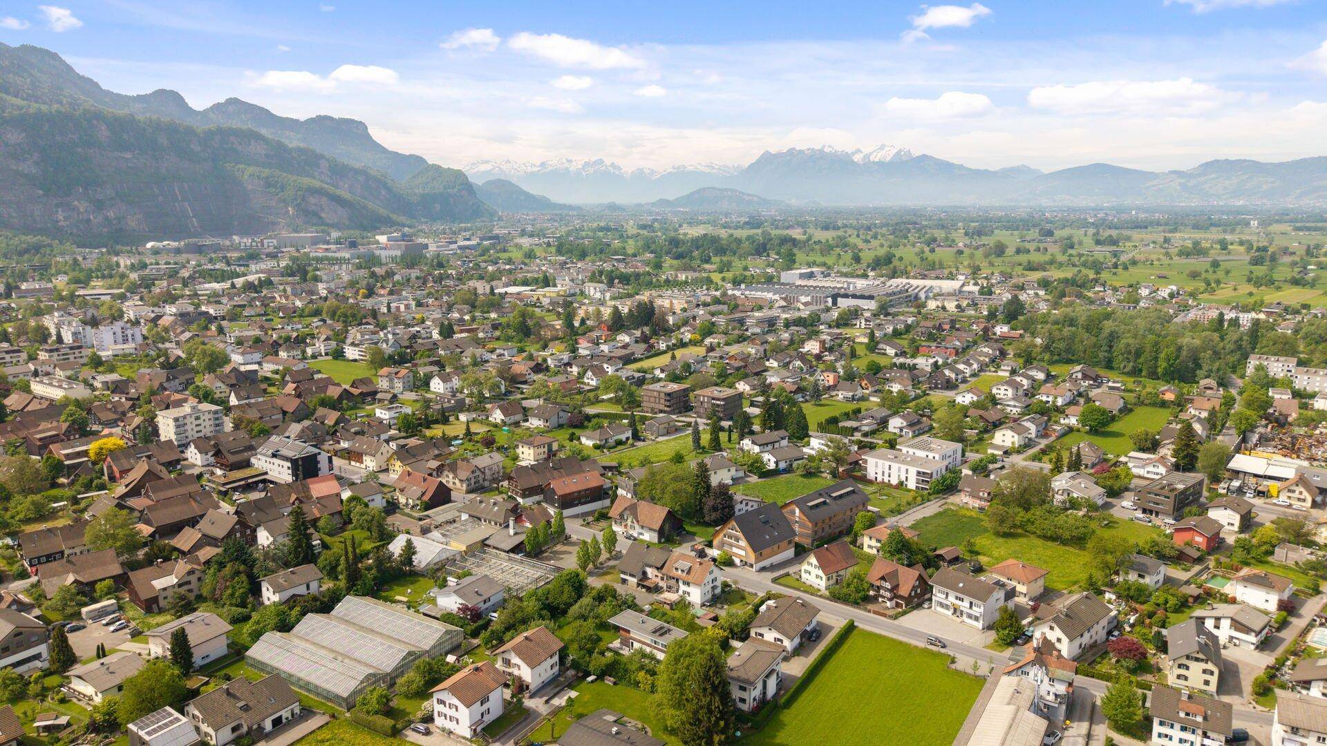 Panoramablick auf eine Stadt mit Wohngebieten und majestätischen Bergen im Hintergrund.
