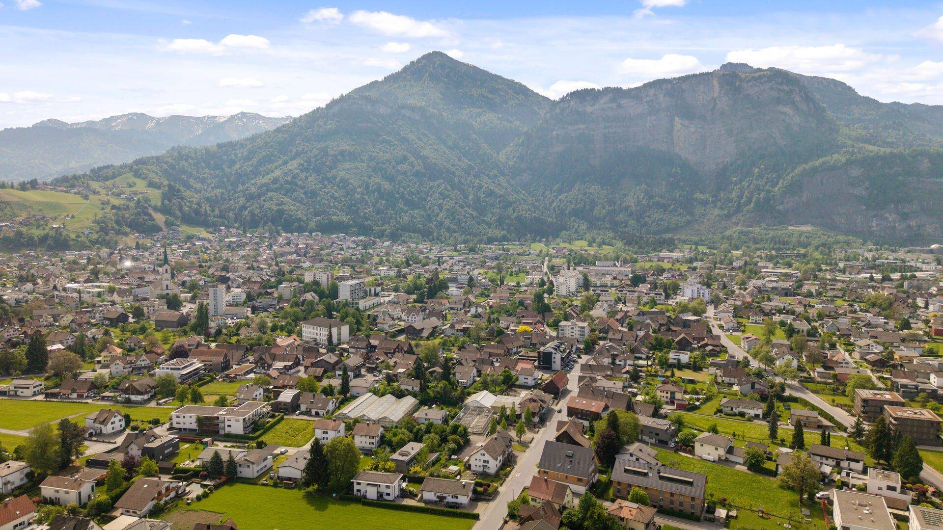 Luftaufnahme einer Stadtlandschaft mit einem markanten Berg und umliegenden grünen Hügeln.