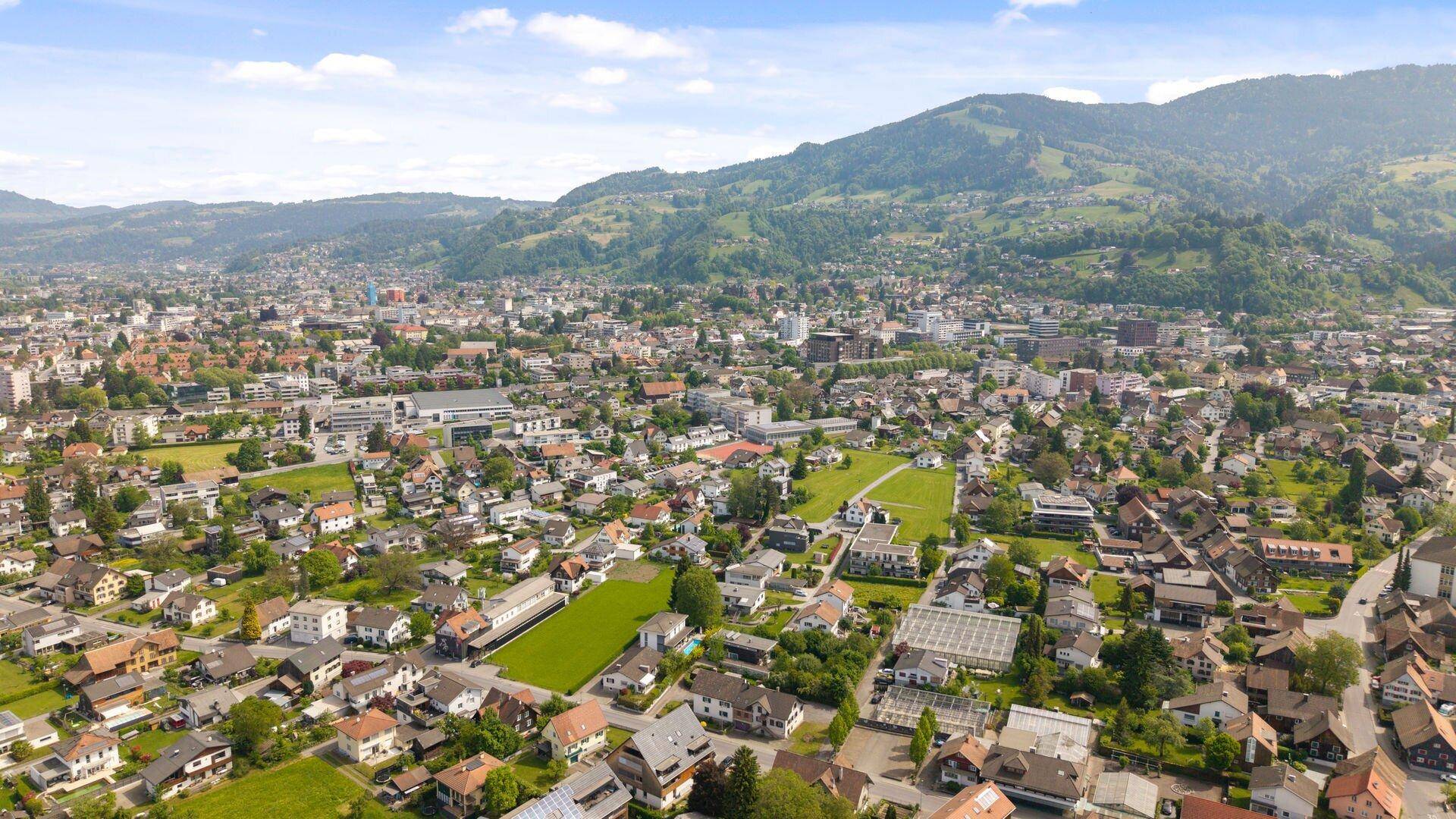 Panoramablick auf eine Stadt mit Wohngebäuden und einer beeindruckenden Bergkulisse.