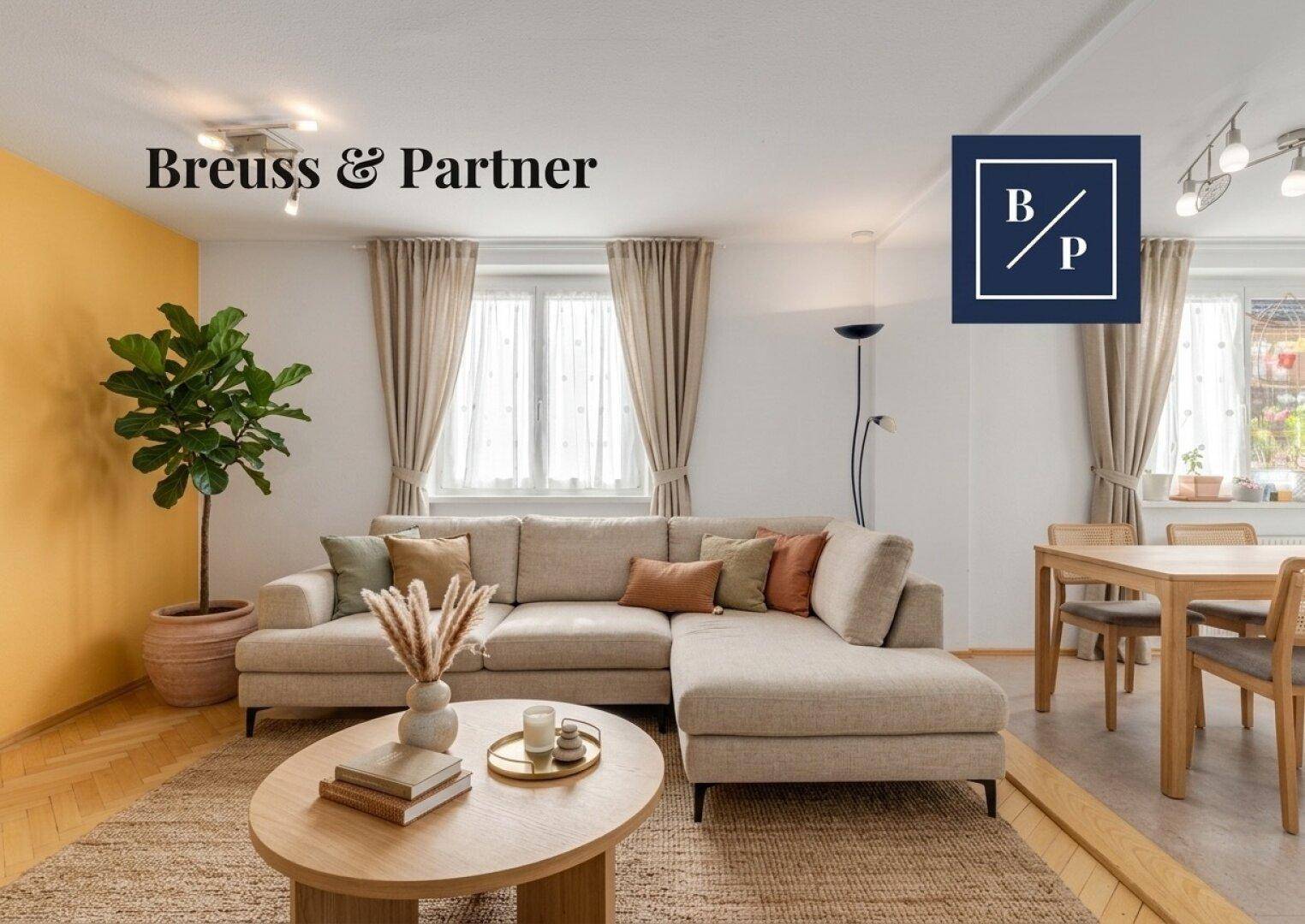 Helles Wohnzimmer mit modernem Ecksofa, Holzboden und Essbereich im Hintergrund.