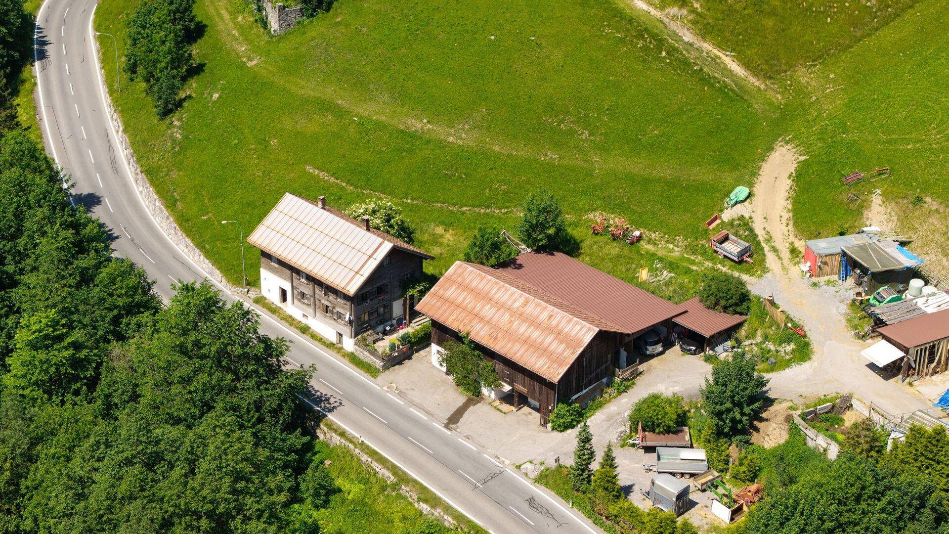 Nahaufnahme von zwei traditionellen Gebäuden mit braunen Dächern, umgeben von einer Landstraße und grünen Hügeln.