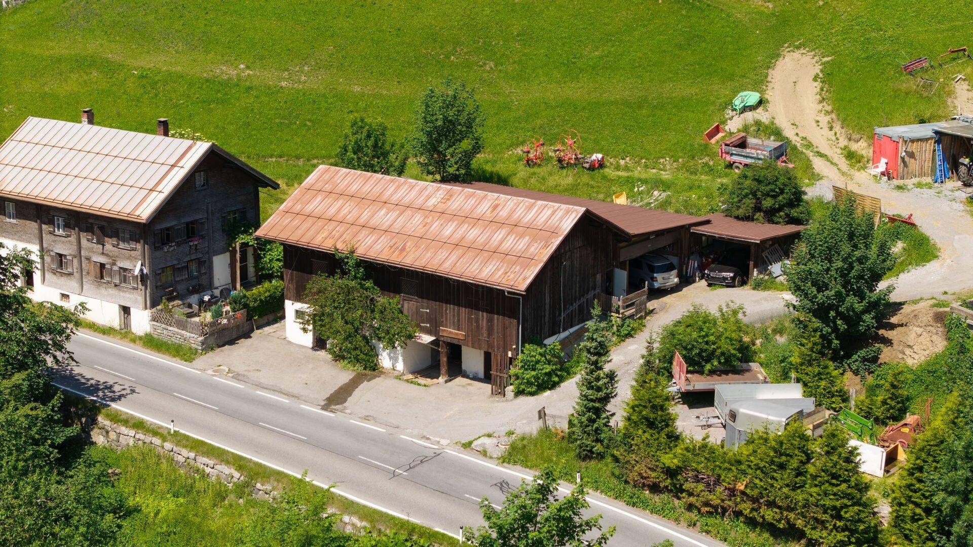 Übersicht aus der Luft mit zwei traditionellen Gebäuden, einer Straße und der umliegenden grünen Landschaft.