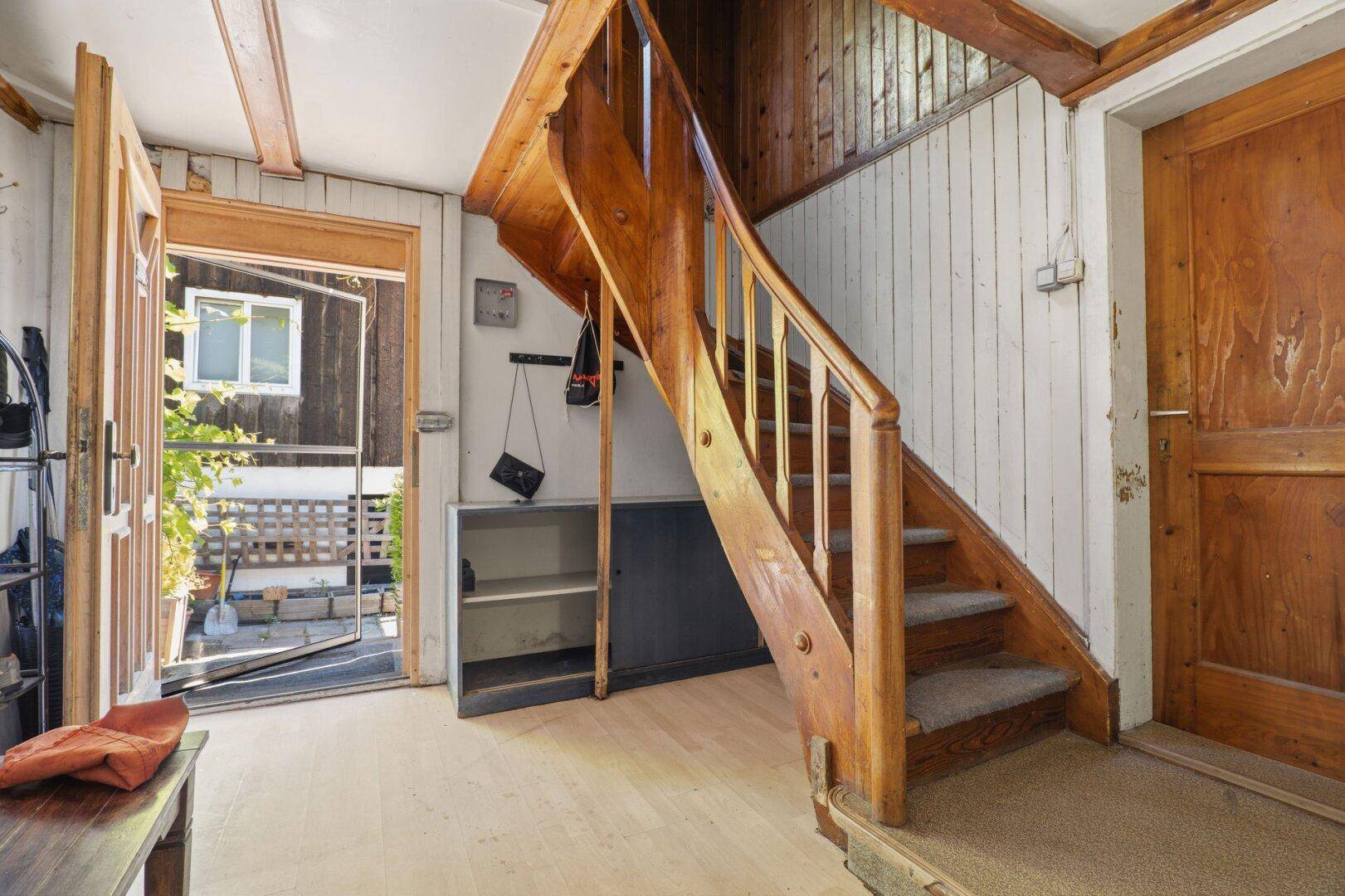 Heller Eingangsbereich mit Holztreppe, Holzvertäfelung und offenem Zugang zum Außenbereich.