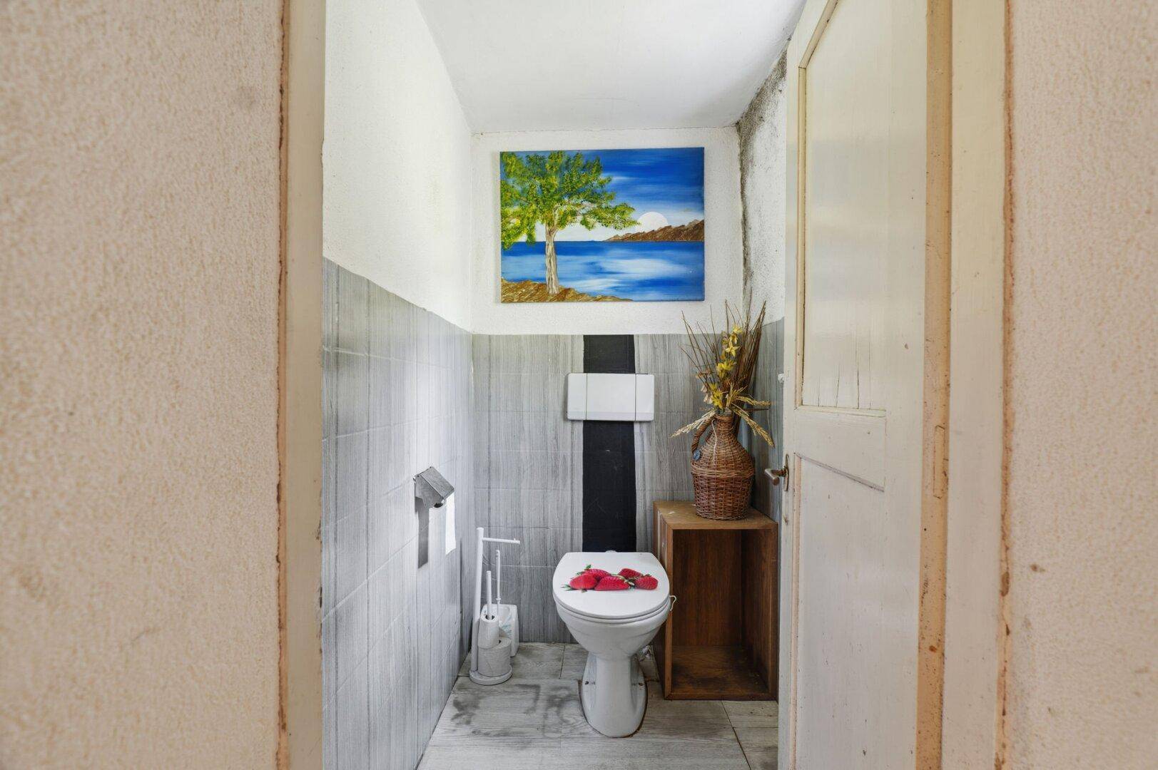 Kleines Gäste-WC mit wandhängender Toilette und grauen Fliesen an den Wänden.