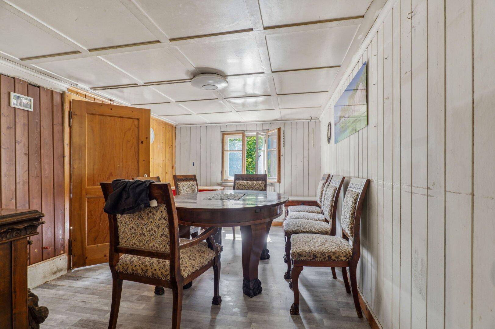 Traditioneller Essbereich mit rundem Holztisch, Stühlen und Holzvertäfelung an einer Wand.