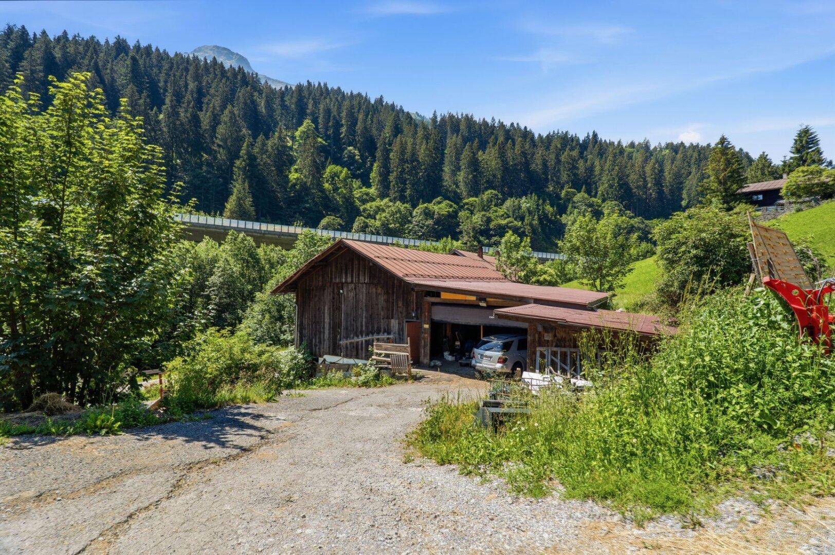 Ansicht eines traditionellen Gebäudes mit offener Garage, umgeben von Bäumen und grünen Hügeln.