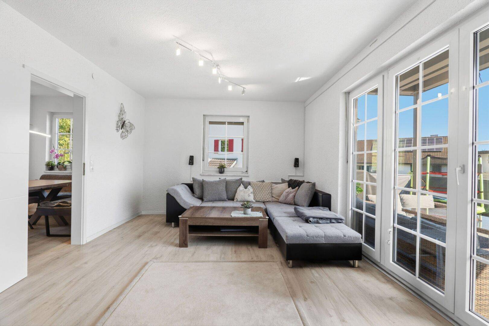 Gemütliches Wohnzimmer mit Ecksofa, hellem Laminatboden und Zugang zur Terrasse.