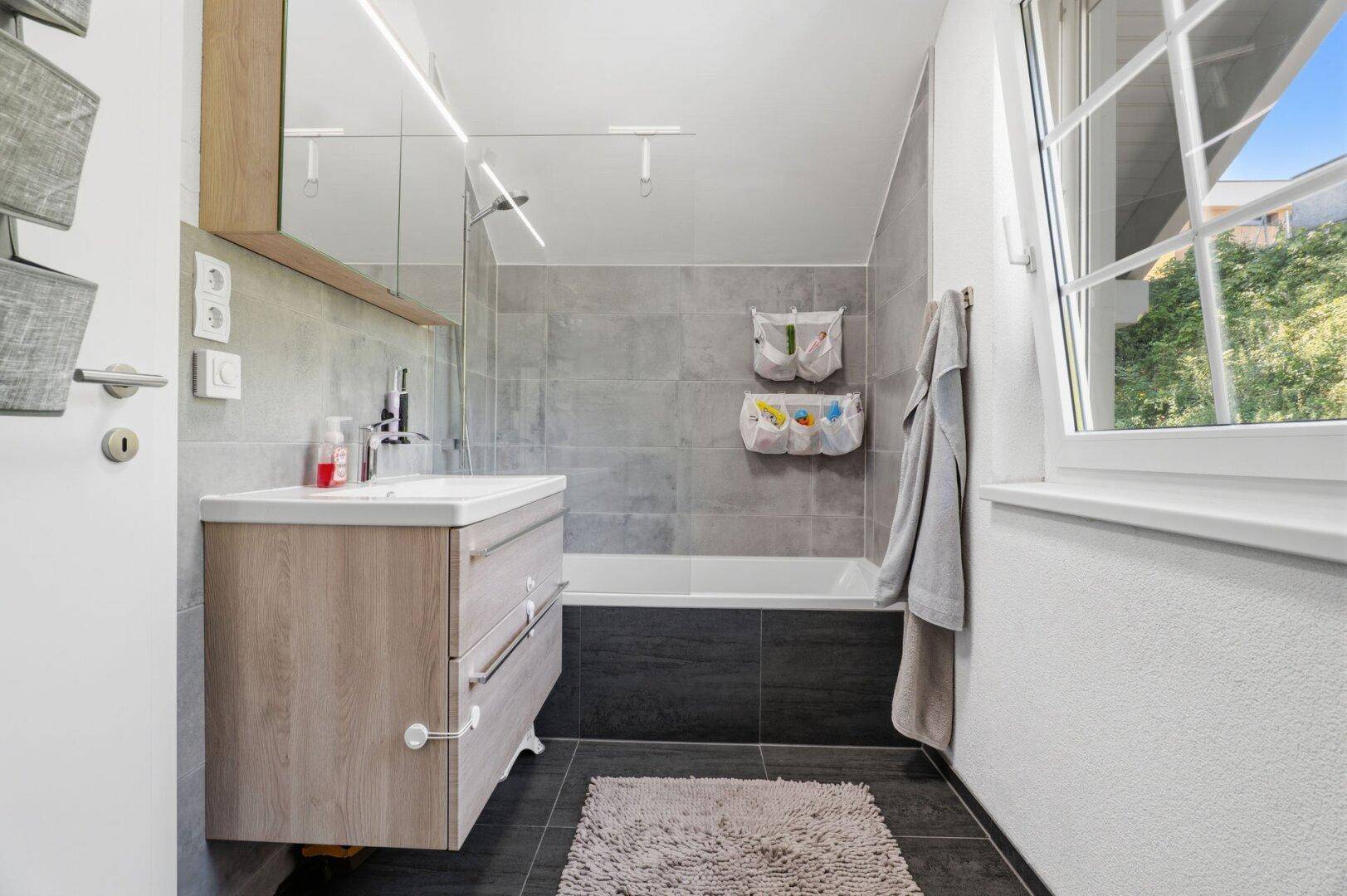Modernes Badezimmer mit Badewanne, Waschtisch und Fenster für Tageslicht.