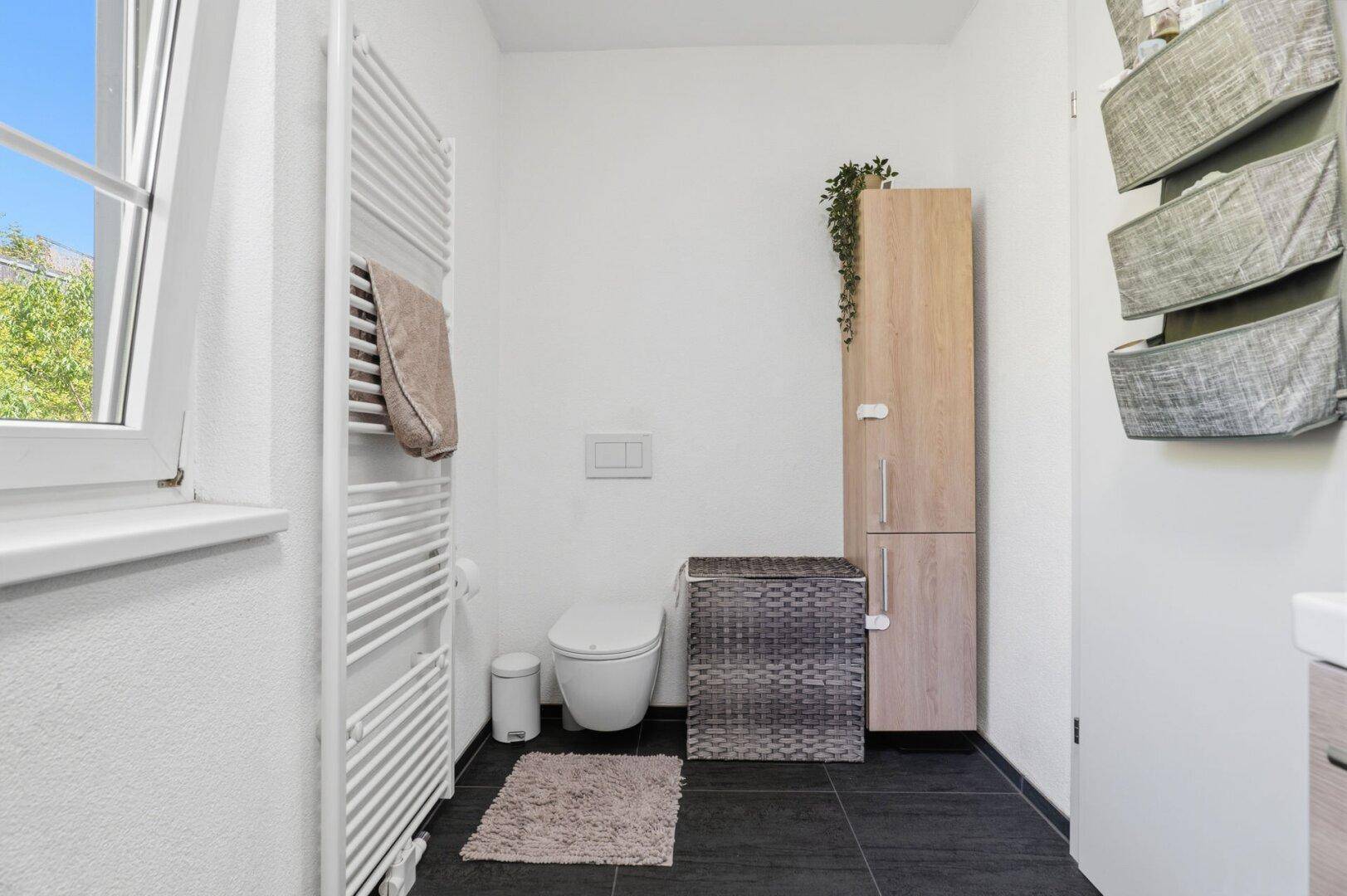 Badezimmer mit wandhängendem WC, beheiztem Handtuchhalter und Fenster.