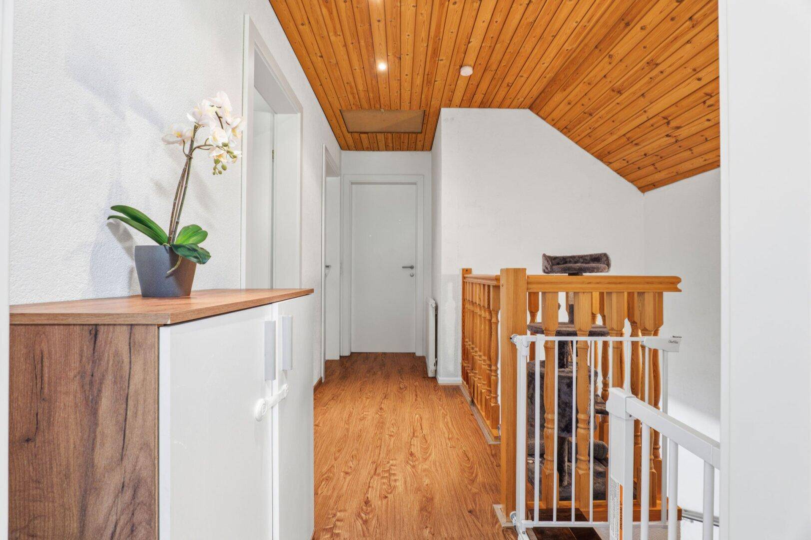Heller Flur im Obergeschoss mit Holzdecke, Laminatboden und Treppengeländer.