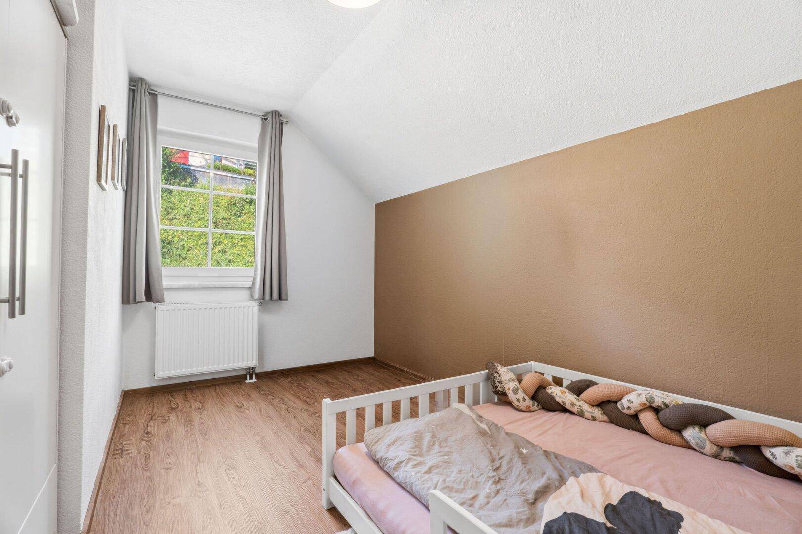 Kinderzimmer mit Laminatboden, Fenster und einer farbigen Akzentwand.
