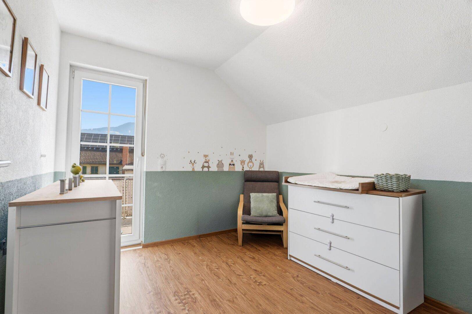Helles Kinderzimmer mit Wickeltisch, Holzboden und Zugang zu einem französischen Balkon.